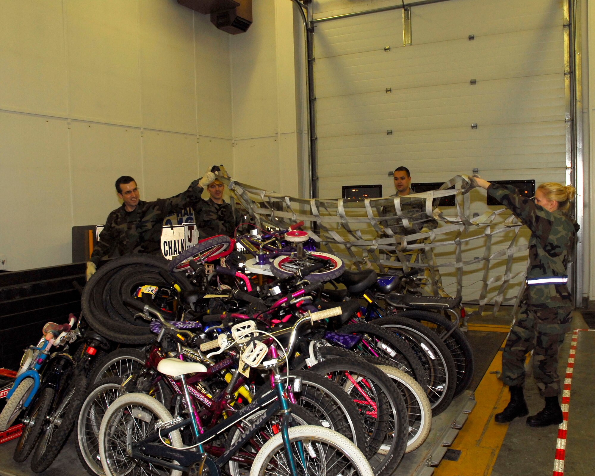 (Left to right) Alaska Air Guardsmen Staff Sgt. Woody Miller, Senior Airman John Darnall, Senior Airman Ryan Pierce and Tech. Sgt. Summer Rehak from the 176th Logistics Readiness Squadron pulls a top net over a pallet of refurbished bicycles on December 6, 2009. The bikes will be airlifted by the Alaska Air National Guard?s144th Airlift Squadron, to Afghanistan to be given to disadvantaged children. (Alaska Air National Guard photo by Tech. Sgt. Shannon Oleson)