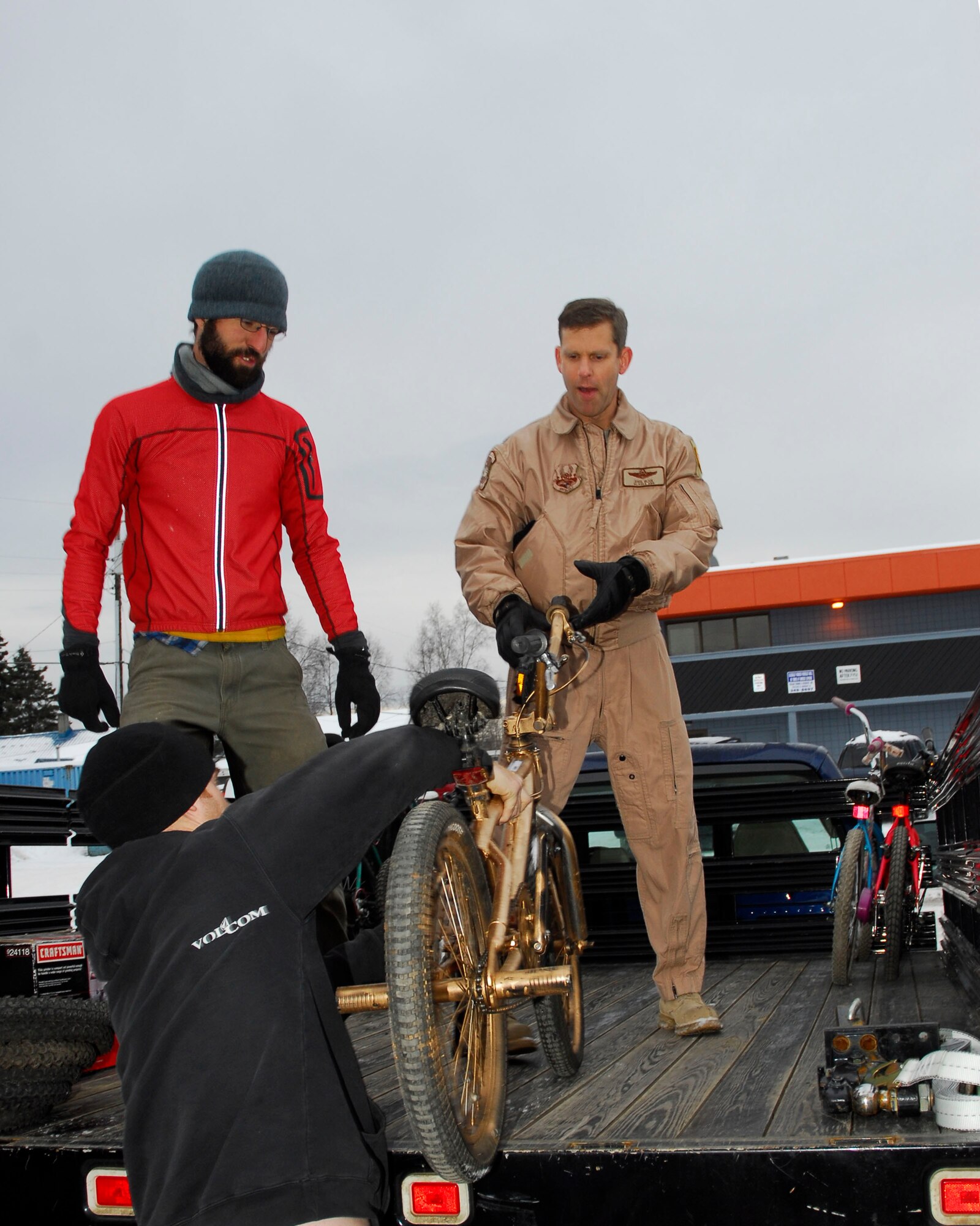 Adam Cosic watches as Henry Crankshaw hands Alaska Air Guardsman Lt. Col. David Glick a bicycle to load onto the truck bed on December 5, 2009.  Cosic and Crankshaw are volunteers at Off the Chain, a bicycle collective, in Anchorage, Alaska.  Glick is a pilot with the 144th Airlift Squadron, Alaska Air National Guard.  The bicycle and twenty-two other refurbished bikes will be airlifted to Afghanistan to be given to disadvantaged children. (Alaska Air National Guard photo by Tech. Sgt. Shannon Oleson)
