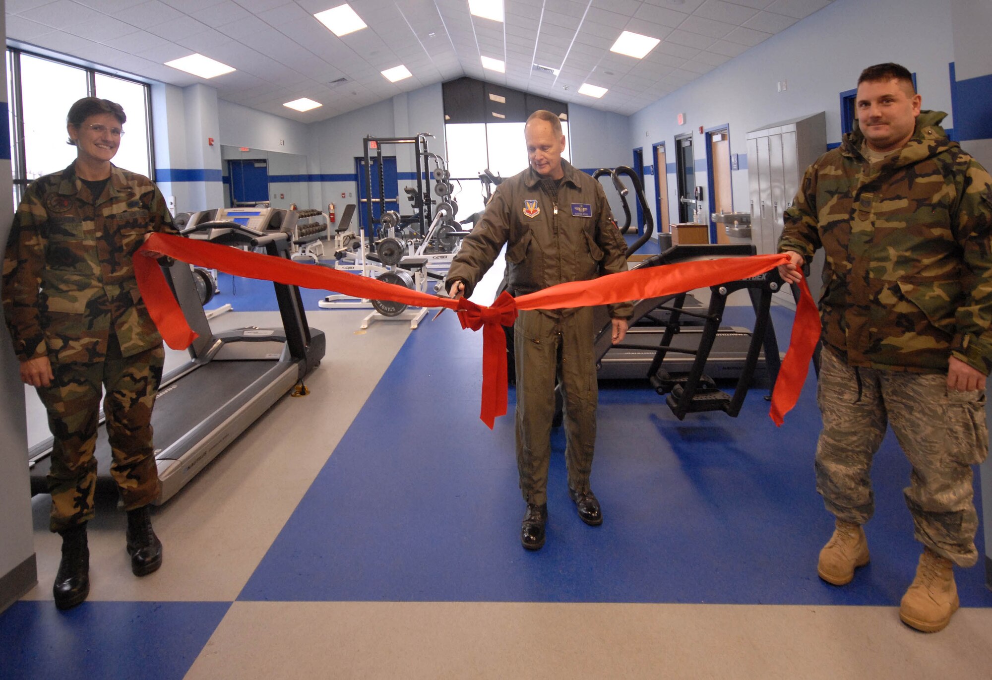 Master Sgt. Carmen LaGuardia, left, and Tech. Sgt. Craig Madden, right , holds the ribbon as Col. Rodger Seidel prepares to cut it during opening ceremonies for the new base gym Friday, Dec, 4, 2009.  The new facility feature more equipment for airman to prepare for the new Air force fitness requirements. (Photo by Master Sgt. Dale Atkins)