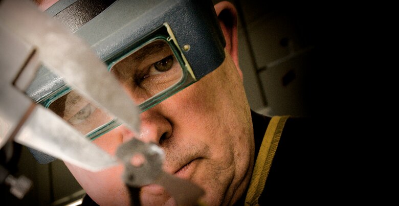 Master Gunsmith William Moore uses a precision binochular visor to magnify the hammer of a Colt 45. The optical visor helps him measure and see imperfections in a weapon's various parts.