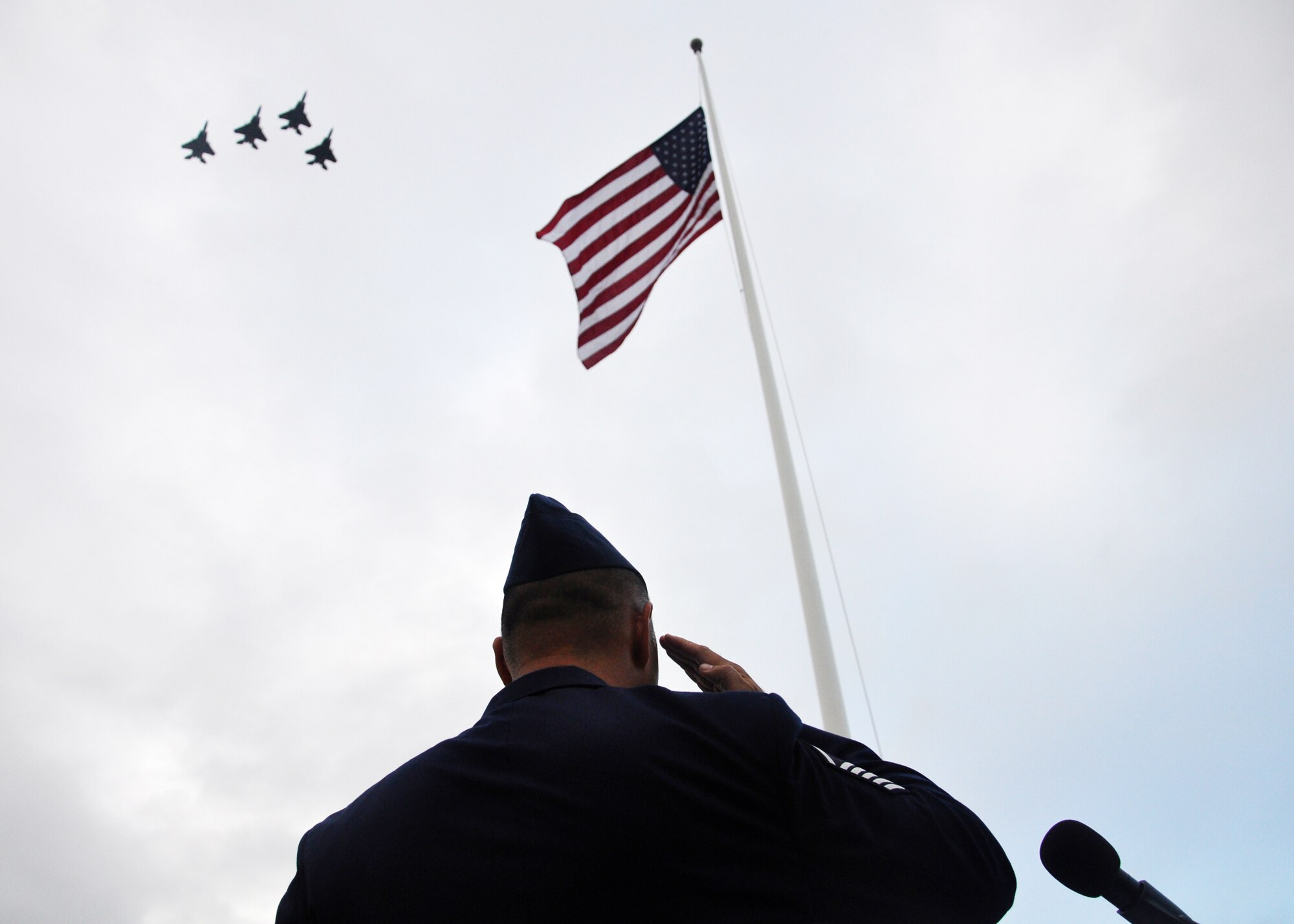 Master Sgt. John Sieh salutes the flag as F-15 Eagles fly a missing man formation Dec. 7, 2009, during the 68th Remembrance Ceremony at Hickam Air Force Base, Hawaii. The ceremony marked the anniversary of the Dec. 7, 1941, attacks on Pearl Harbor Navy fleet and the Army Air Corps fields of Hickam, Wheeler and Bellows. Sergeant Sieh is from the 15th Airlift Wing protocol office and the F-15s are from the 199th Fighter Squadron, Hawaii Air National Guard. (U.S. Air Force photo/Staff Sgt. Mike Meares)