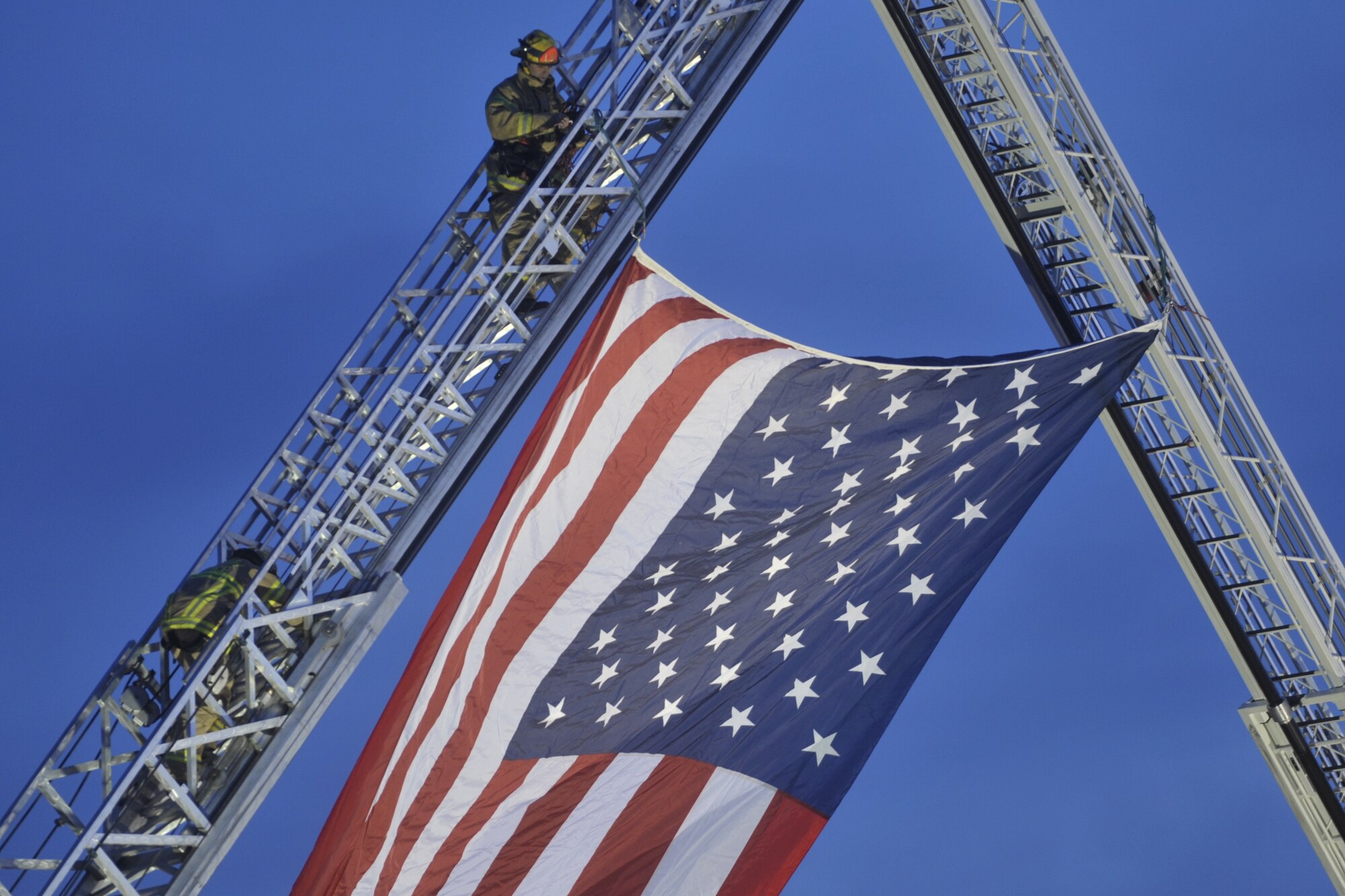 Lakewood emergency responders hang the flag from fire truck ladders at the McChord north gate where approximately 2,000 emergency services vehicles from throughout the U.S. and Canada are staging their vehicles to depart McChord Dec. 8 in a procession to the Tacoma Dome Memorial Service honoring four fallen Lakewood, Wash., Police Officers. (U.S. Air Force photo/Abner Guzman)