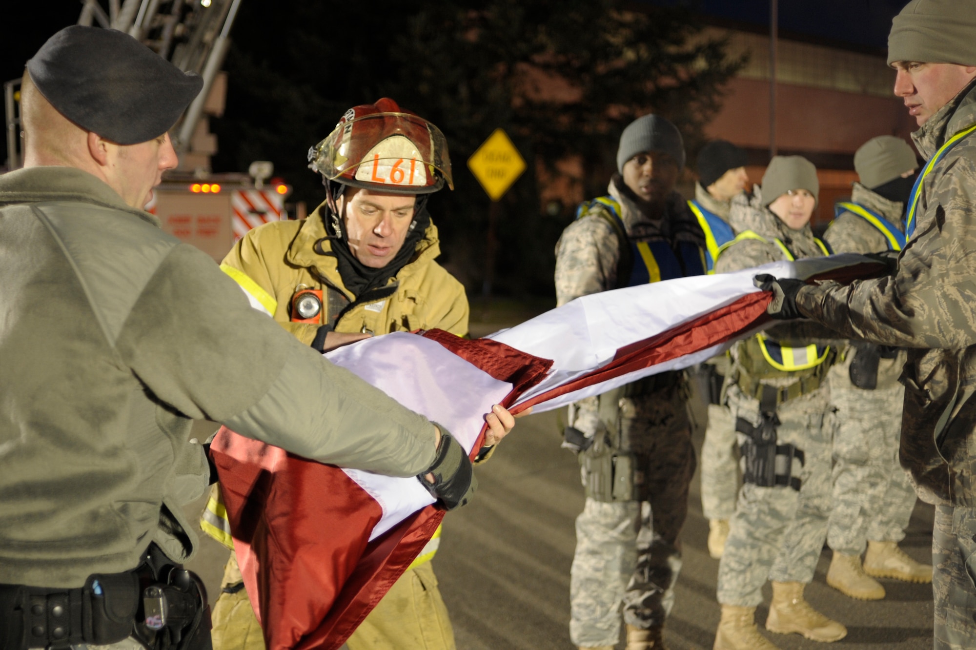 McChord Airmen and Lakewood emergency responders unfold the flag they will hang from fire truck ladders over the McChord north gate where approximately 2,000 emergency services vehicles from throughout the U.S. and Canada are staging their vehicles to depart McChord Dec. 8 in a procession to the Tacoma Dome Memorial Service honoring four fallen Lakewood, Wash., Police Officers. (U.S. Air Force/Abner Guzman)