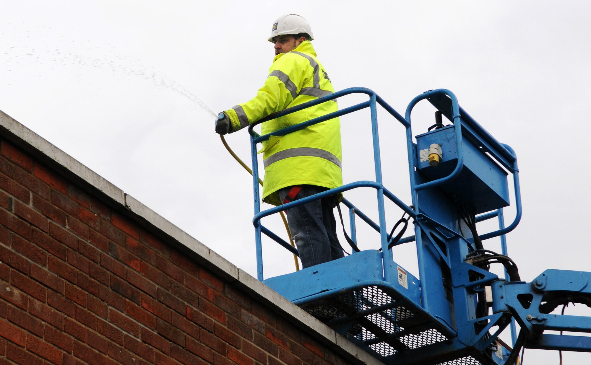 RAF MILDENHALL, England -- John Milton, a local contractor, covers the roof of the Auto Skills Development Center here with water to check for leaks from the basket of an articulating boom. Workers were concerned that leaking water from recent rainfall was getting inside and posing a slipping hazard for mechanics. The contractors checked the integrity of roof vent seals by soaking them with water from a nearby hydrant and examining the work areas inside the building. (U.S. Air Force photo/Senior Airman Thomas Trower)