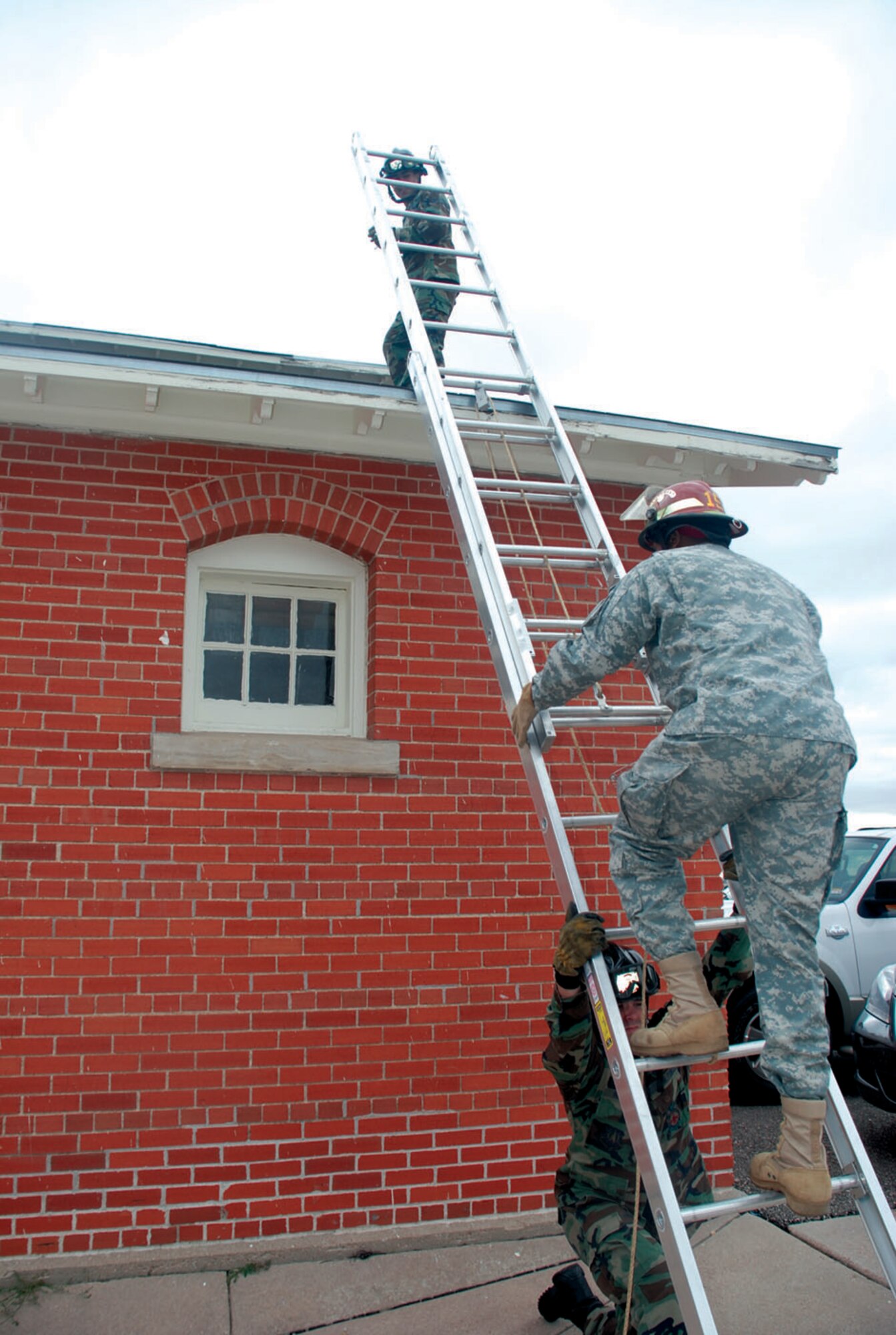 Airman 1st Class Calvin Wayman, 90th Civil Engineer Squadron fire department, braces the ladder as Airman 1st Class Migeul Rodriguez, 90th CES fire department, and Army Sgt. David Smith, veterinarian technician, climb to the roof to rescue Tiger. Once in position, Airman Rodriguez blocked the pathway Tiger may have run to, and Sergeant Smith quickly grabbed the cat.