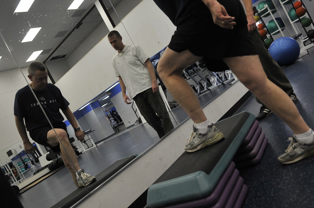 Brian Williams, Brian Williams, Health and Wellness Center exercise physiologist,, watches as Lt. Col. (Chaplain) David Wilshek, 11th Wing Chaplain, performs step-ups during a physical therapy appointment Dec. 3 at the Bolling Air Force Base Gym. Chaplain Wilshek requires physical therapy after developing Runner’s Knee from running four to six miles seven times a week for 35 years. (U.S. Air Force photo by Senior Airman Marleah Miller)