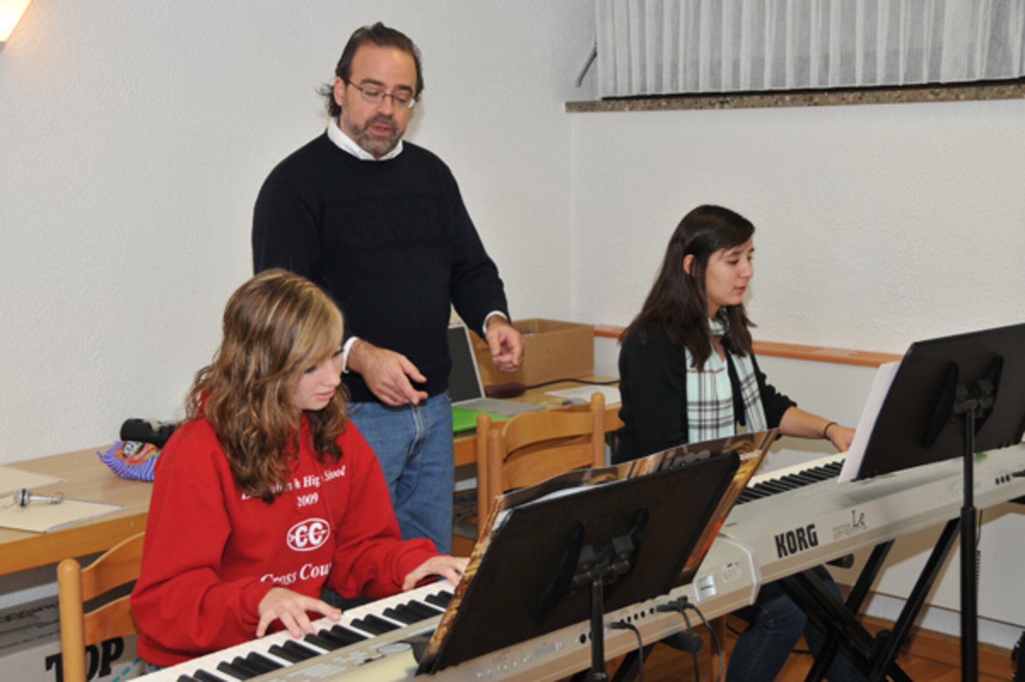 Mr. Cary Sand, Air Force North High School music instructor, discusses technique with Rachel Cranney and Elysia Garcia, Lakenheath High School, pianists. The pianists accompany the strings group at Creative Connections. 