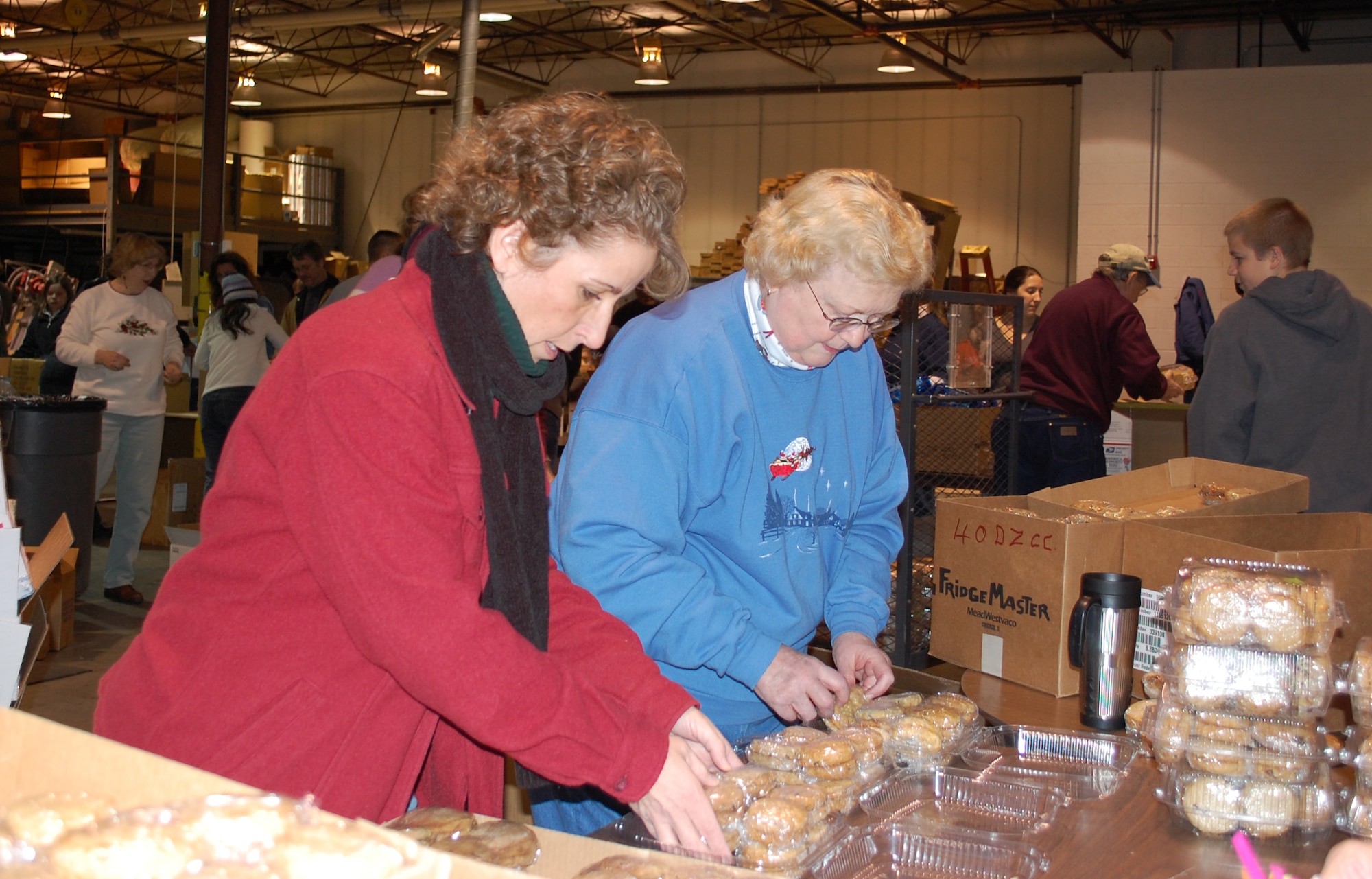 Chief Master Sgt. Cari Kent, 341st Missile Wing command chief master sergeant, and Penny Kubick, long-time volunteer, pack containers with homemade chocolate chip, peanut butter and oatmeal raisin cookies Dec. 5. The containers are one of many items added to Operation Happy Holiday care packages, being assembled by more volunteersin the background. The group put together 200 packages to be shipped to deployed Montana servicemembers in time for the holdiays. (U.S. Air Force photo/Valerie Mullett)