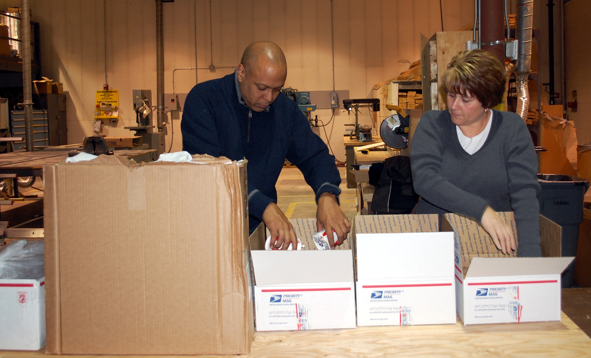 Col. Anthony Cotton, 341st Missile Wing vice commander, adds two cups of hard candies to care pacakges Dec. 5. Family member Wendy Harley waits to get candy added to her two boxes before taking them on to the next stop in the assembly line-like box packing operation. (U.S. Air Force photo/Valerie Mullett)