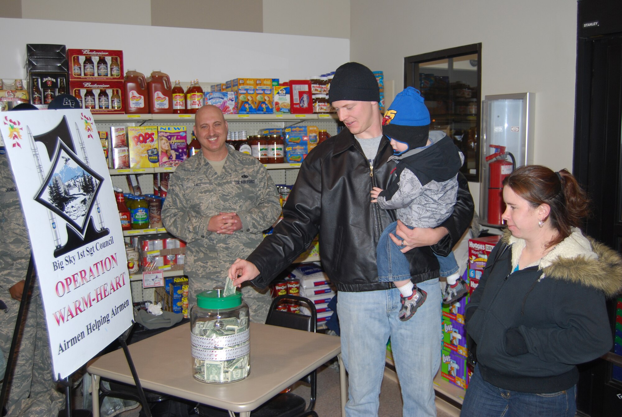 Staff Sergeant Allen Rolfe, 741st Missile Security Forces Squadron response force leader, donates to Operation Warm Heart on his weekly trip to the commissary with his wife, Ashley, and his son, Braden, 2. OWH is a program managed by Team Malmstrom’s First Sergeants Council geared towards helping Airmen and their families undergoing financial hardships by providing them with grants to support them in their time of need. Master Sgt. Jason Hill, 341st Logistics Readiness Squadron first sergeant, looks on. (U.S. Air Force photo/Airman 1st Class Kristina Overton)