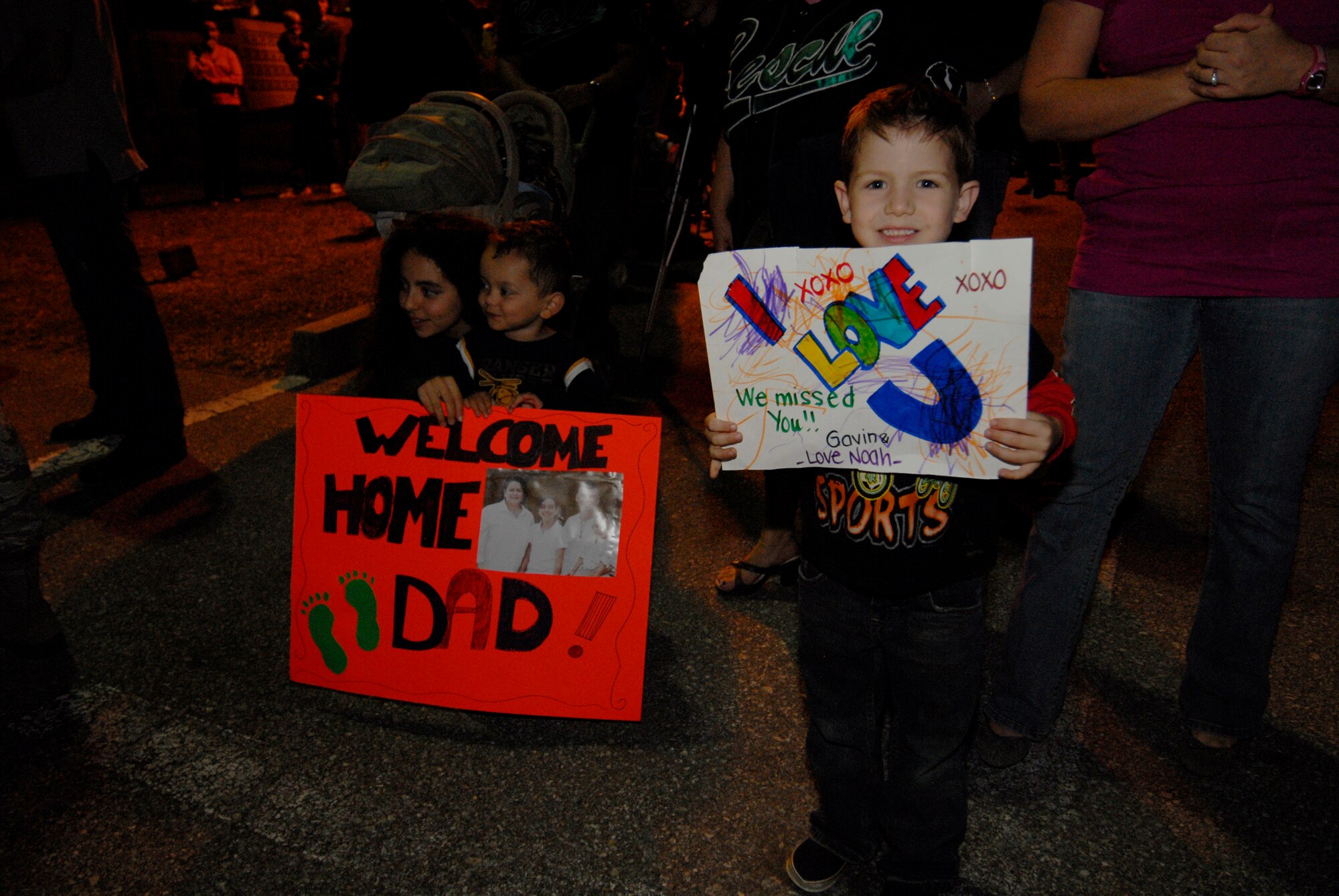 Vicky and Brandon Ray, children of Master Sgt. James Ray of the 33rd Rescue Squadron, and Gavin Lesieur, son of Staff Sgt. Jason Lesieur of the 718th Aircraft Maintenance Squadron, hold up signs for their dads returning from a deployment to Afghanistan Dec. 8. Dozens of friends and family members gathered outside Kadena's passenger terminal to welcome more than 60 Kadena Airmen as they returned from a deployment supporting Operation Enduring Freedom. (U.S. Air Force/Airman 1st Class Chad Warren)