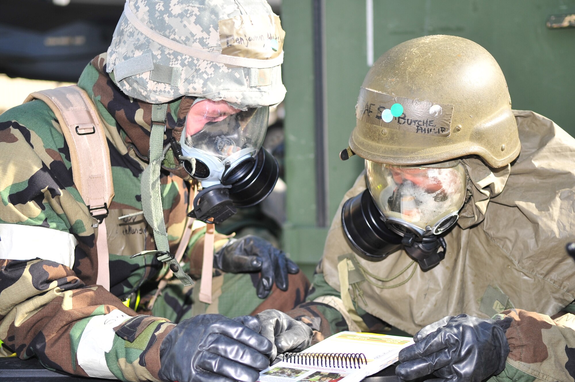 Airman Benjamin Hutchens and Senior Airman Phillip Butche, 4th Aircraft Maintenance Squadron, review their Airman's Manual after a simulated chemical attack on the flightline during an oerational radiness eercise on Seymour Johnson Air Force Base, N.C., Dec. 10, 2009. Both Airmen are in mission-oriented protective posture level four, which requires them to wear a special suit, rubber over-boots, an MCU-2 gas mask and rubber gloves. (U.S. Air Force photo/Airman 1st Class Rae Perry)