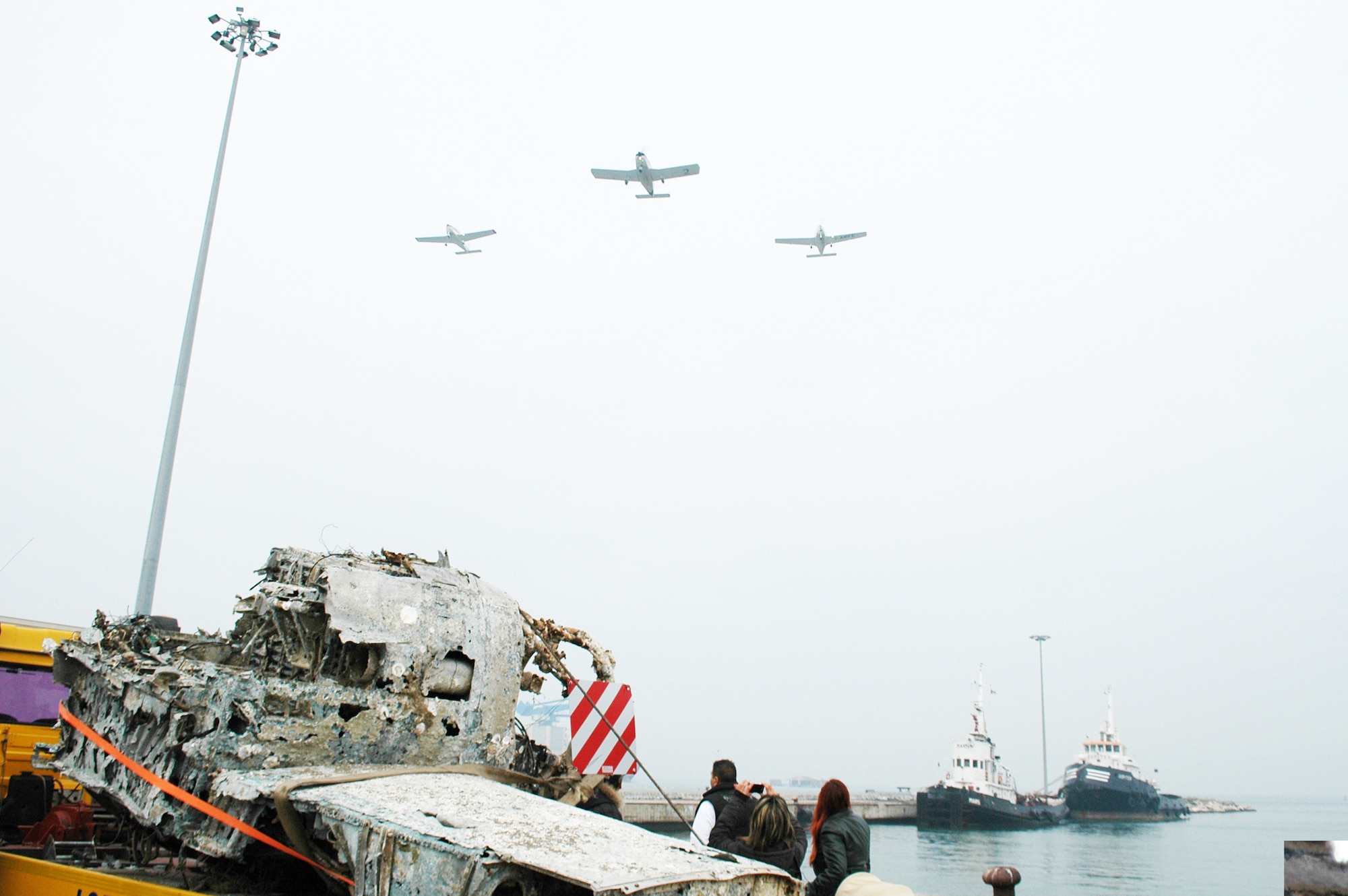 An Italian fisherman and his family look on as an Italian aero club performs a ceremonial fly-over during a ceremony Nov. 14, 2009, in Chioggia, Italy. The ceremony honored the unknown pilot and other pilots past and present, and transferred the wreckage believed to be that of a P-47 Thunderbolt recovered from the bottom of the Adriatic Sea May 12, 2009, to an Italian aero club who will begin a restoration project expected to take two years. (U.S. Air Force photo/Tech. Sgt. Michael O'Connor)