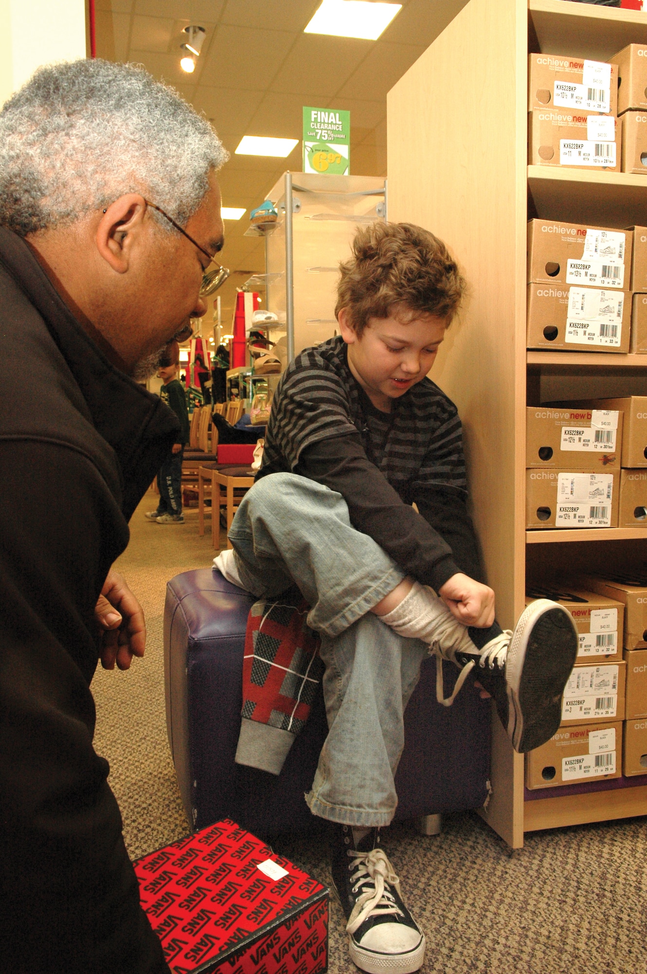 Braden Brandon, 10 gets ready to try on a new pair of shoes with the help of volunteer Gerald Joseph, 727th Aircraft Sustainment Group. Braden was one of 27 children that 727th volunteers took shopping at a local department store Dec. 4. Volunteers from the group raised money throughout the year and linked up with a local elementary school to buy clothes, shoes and jackets for children in need. Volunteers from the 727th have been holding the program for the past 18 years. (Air Force photo by Micah Garbarino)
