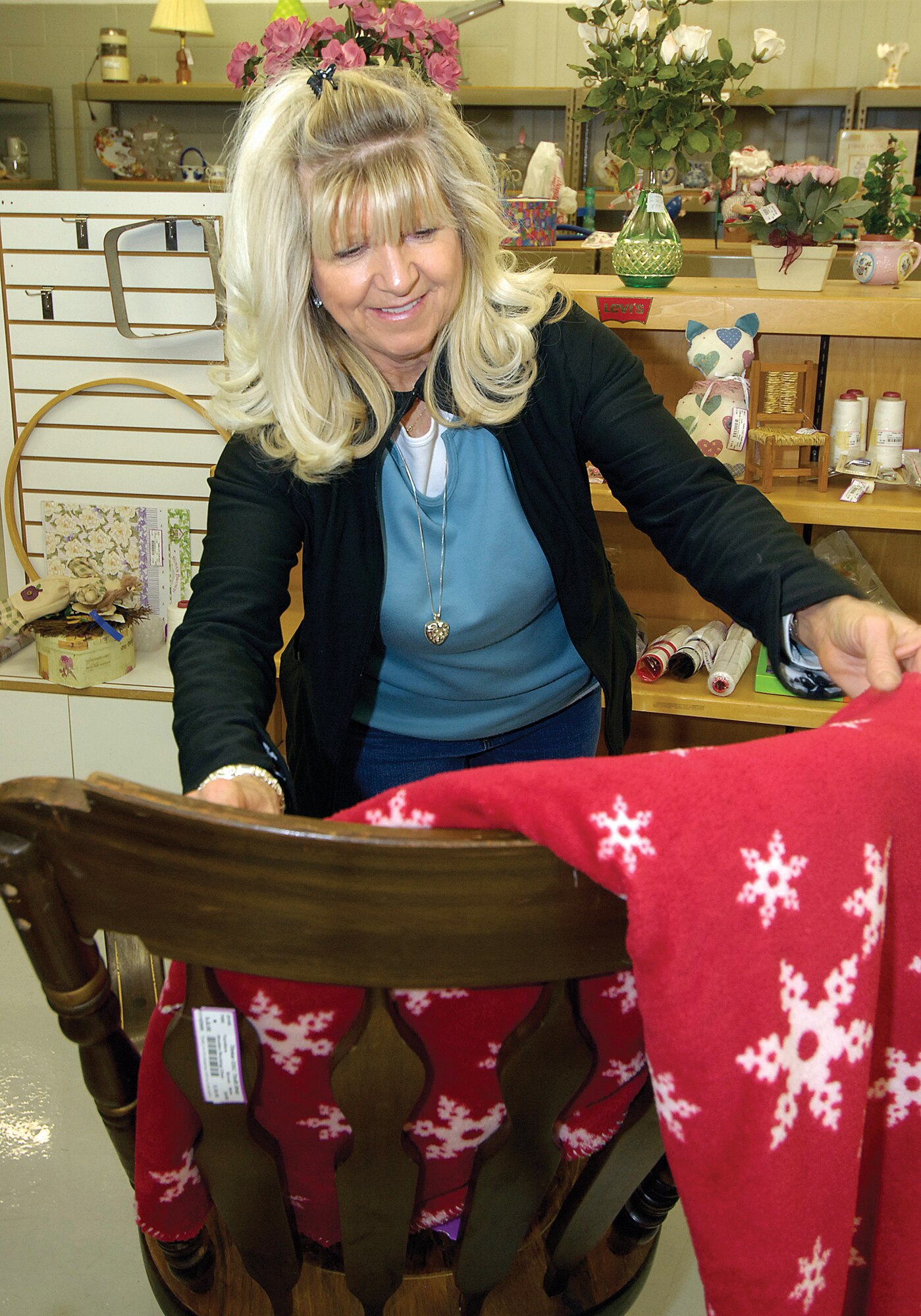 Tinker Thrift Shop volunteer Janie Hardin makes a holiday throw and a wooden rocker more inviting for potential shoppers in the thrift shop’s furniture area recently.  Ms. Hardin consigned items for years then became a volunteer in the shop more than four years ago. (Air Force photos by Margo Wright )