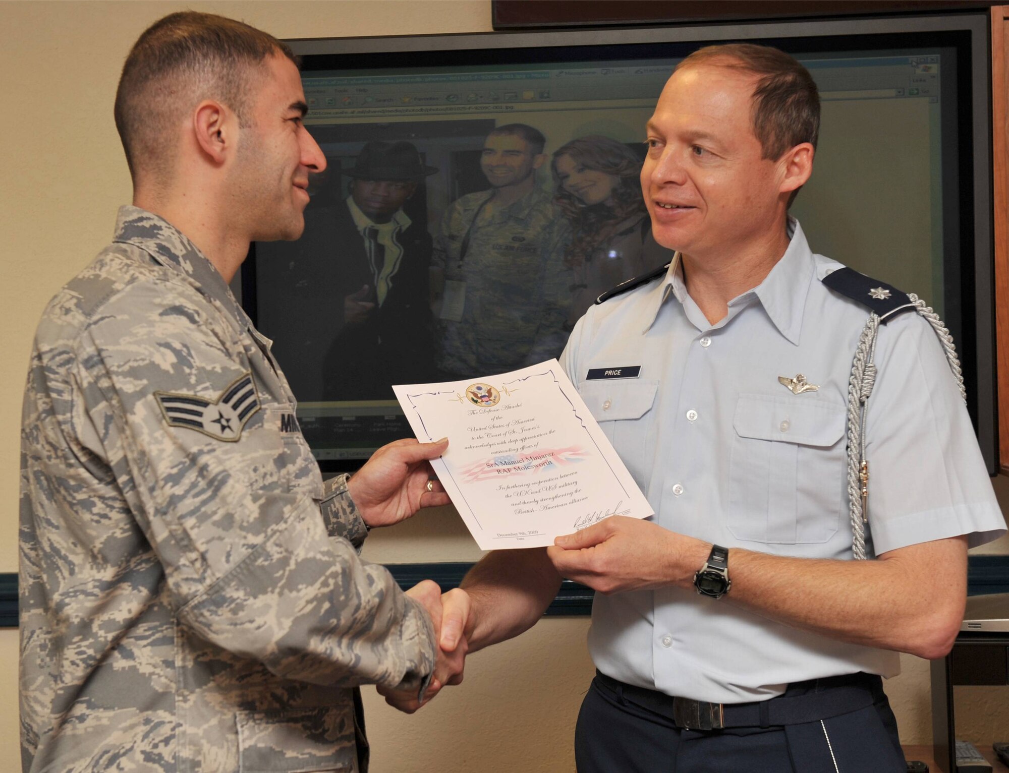 AFRICOM IKD-Molesworth Senior Airman Manuel Minjarez receives a Certificate from the Defense Attaché Office, London. Assistant Air Attaché Lt. Col Jeffrey K. Price noted that Minjarez demonstrated leadership and diplomacy in facilitating the U.S. and U.K. Honor Guard presentation at the recent NFL game in London.  In the background photo, Minjarez meets singers Ne-Yo and Joss Stone also performing at the game. (U.S. Air Force photo by Staff Sgt. Javier Cruz)