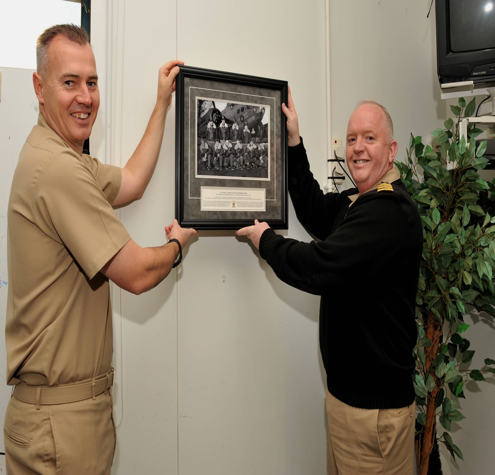 JAC Deputy Commander, Navy Capt. Henry J. "Harry" Babin, and JAC Senior Enlisted Leader, Navy Master Chief John C. Frakes hang a photograph 4 December of the 1st Lt. Vern L.Moncur crew at Molesworth.  The photo was taken 66 years earlier to the day in 1943.  The photo hangs in the JAC Thunderbird Lounge.  (U.S. Air Force Photo by Staff Sgt. Javier Cruz)