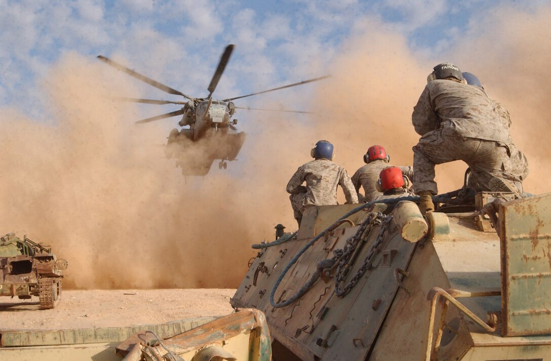 With a wall of sandy rotor-wash before them, Helicopter Support Team Marines with Landing Support Company, Combat Service Support Battalion 7, 1st Force Service Support Group, watch for the approach of a CH-53E Super Stallion from Marine Medium Helicopter Squadron 166 (reinforced), Marine Aircraft Group 16, Jan. 9 while sitting on an old Iraqi armored personnel carrier. The Marines were waiting to conduct one of many external lifts of the vehicles that were moved from Al Asad, Iraq to an off-base shooting range used by aircraft from 3rd Marine Aircraft Wing. Photo by Cpl. Paul Leicht