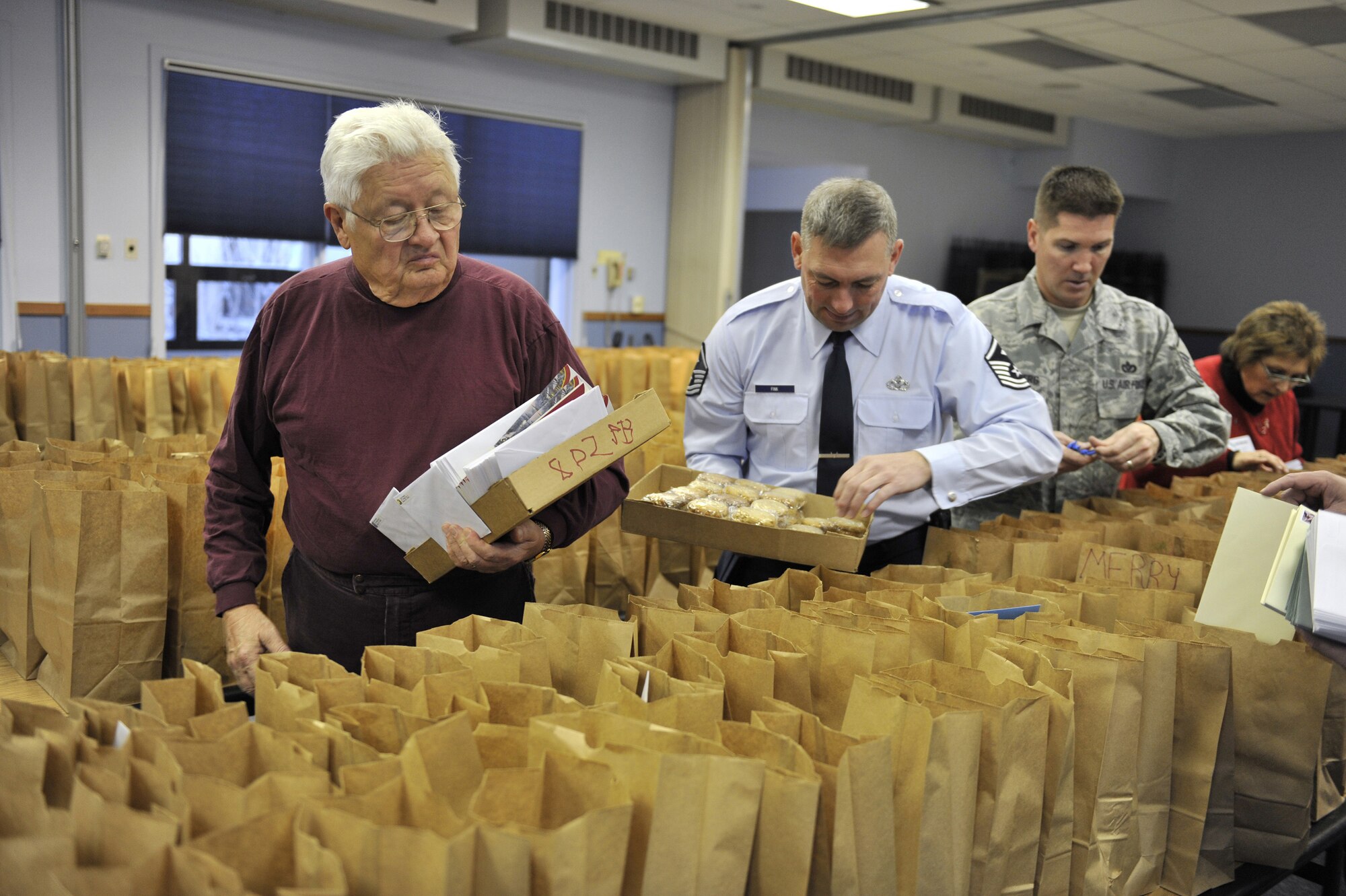 Steve Kubick (front) and Dimmer Kjelsrud (back) assist Master Sgt. Scott Fink, 341st Force Support Squadron first sergeant and Master Sgt. Paul Sassenberg, 341st Civil Engineer Squadron Engineering Superintendent with packing holiday bags for dormitory residents Dec. 7. Each year as part of Operation Happy Holidays, which Mr. Kubick founded 11 years ago, volunteers bake cookies to send to deployed members with enough left overto support  this program, called Operation Cookie Express, for Malmstrom's single Airmen. (U.S. Air Force photo/John Turner)