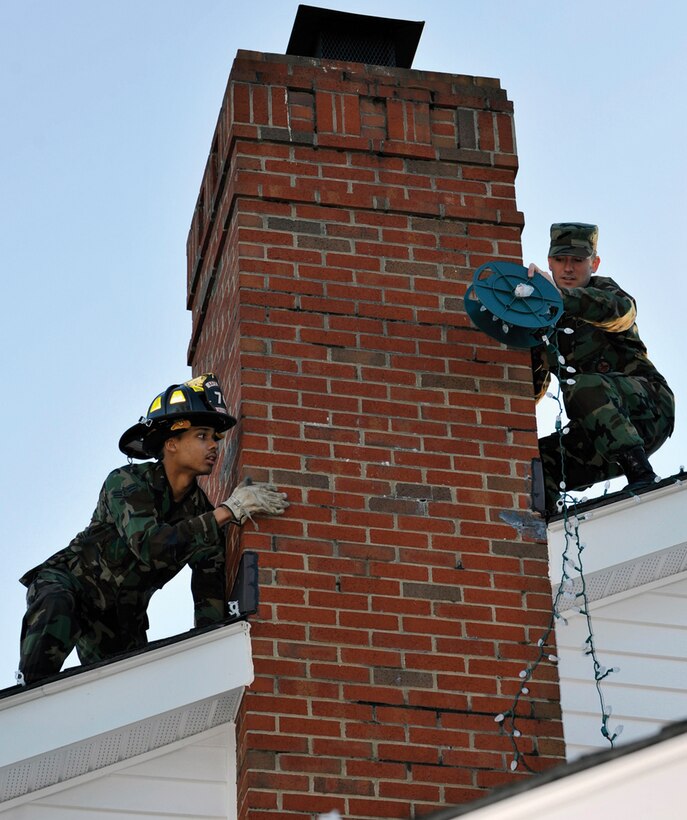 Staff Sgt. Robert Cook, 316th Civil Engineer Squadron firefighter, passes a roll of holiday lights to Airman 1st Class Christopher Hale, 316 CES firefighter, on the roof of the Fisher House Wednesday. Firefighters spent the day decorating the Fisher house, a place where families of wounded warriors can stay while awaiting medical treatment. (U.S. Air Force photo/ Airman 1st Class Perry Aston)