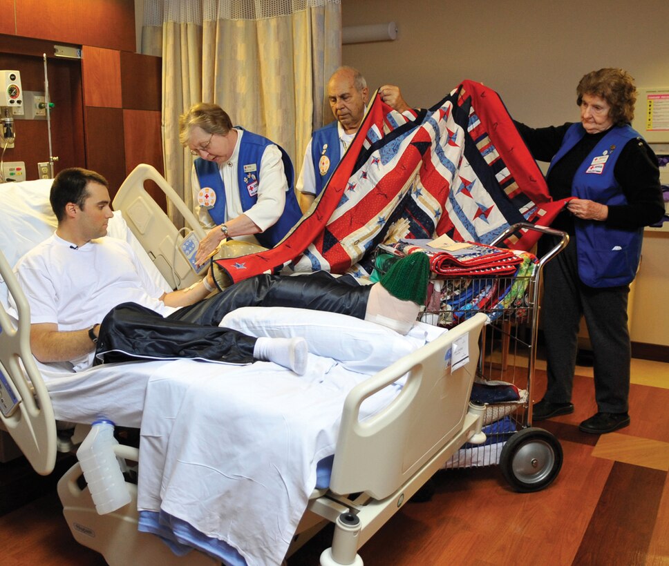 Felicia Hilleary, Lt. Col. (ret.) Denny Politano and Maj. (ret.) Charlotte Politano give a hand-sewn, donated quilt to Private 1st Class Jonathan Winker, Army National Guard member and returning Soldier from Iraq, Dec. 1 at Malcolm Grow Medical Center. CNN crew members were on location at the Aeromedical Staging Facility to film part of a television special on the journey that these quilts take from their creator to the wounded or injured servicemembers who receive them. (U.S. Air Force photo/ Staff Sgt. Renae Kleckner)