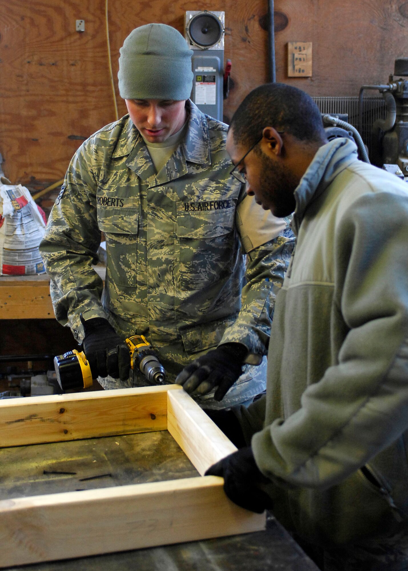 BAGRAM AIRFIELD, Afghanistan -- Senior Airman Matthew Roberts (left) and Airman 1st Class Michael Carey (right), force protection Airmen from the 455th Expeditionary Civil Engineering Squadron, work together to connect two pieces of plywood while building shelves for the laundry services office, Dec. 11, 2009.  The shelves will be use to hold laundry waiting to be picked up by the growing population of Airmen.  Airman Roberts is deployed from Elmendorf Air Force Base, Alaska and hails from Hartford, Mich.  Airman Carey is deployed from Eglin AFB, Fla., and hails from Augusta, Ga.  (U.S. Air Force photo/Senior Airman Felicia Juenke)