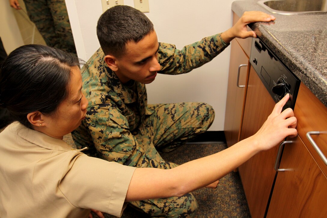 Lt. Cmdr. Leah Y. Geislinger, assistant department head, Physical and Occupational Therapy Department, Naval Hospital Camp Pendleton, walks Lance Cpl. Emilio A. Vasquez, one of the first two ADL apartment patients with 1st Supply Battalion, 1st Marine Logistics Group, through proper dishwashing steps at the opening of the Marine Corps’ first rehabilitation apartment at Camp Pendleton’s Naval Hospital, Dec. 11.
