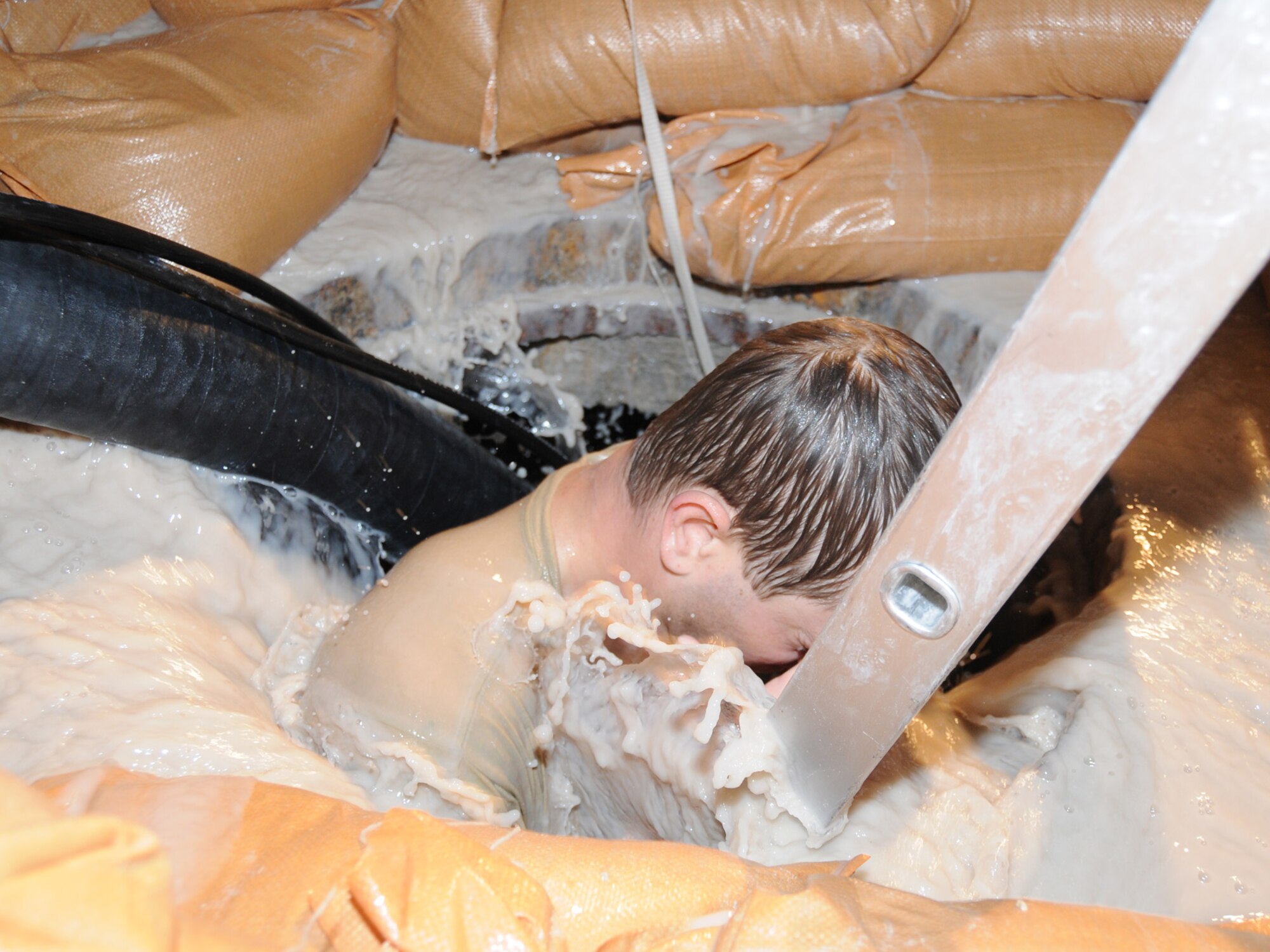 Senior Airman Bo Brauer, 379th Expeditionary Communications Squadron cable and antenna maintenance technician, descends into a flooding manhole to perform emergency repair on severed cables at a deployed location in Southwest Asia, Dec. 14, 2009. The base, which is located in an area that typically receives an average of 1.9 inches of rain annually, has received 1.06 inches in the last 24 hours. Airman Brauer is deployed from Ramstein Air Base, Germany, in support of operations Iraqi Freedom and Enduring Freedom. (U.S. Air Force Photo/Tech. Sgt. Jason W. Edwards)