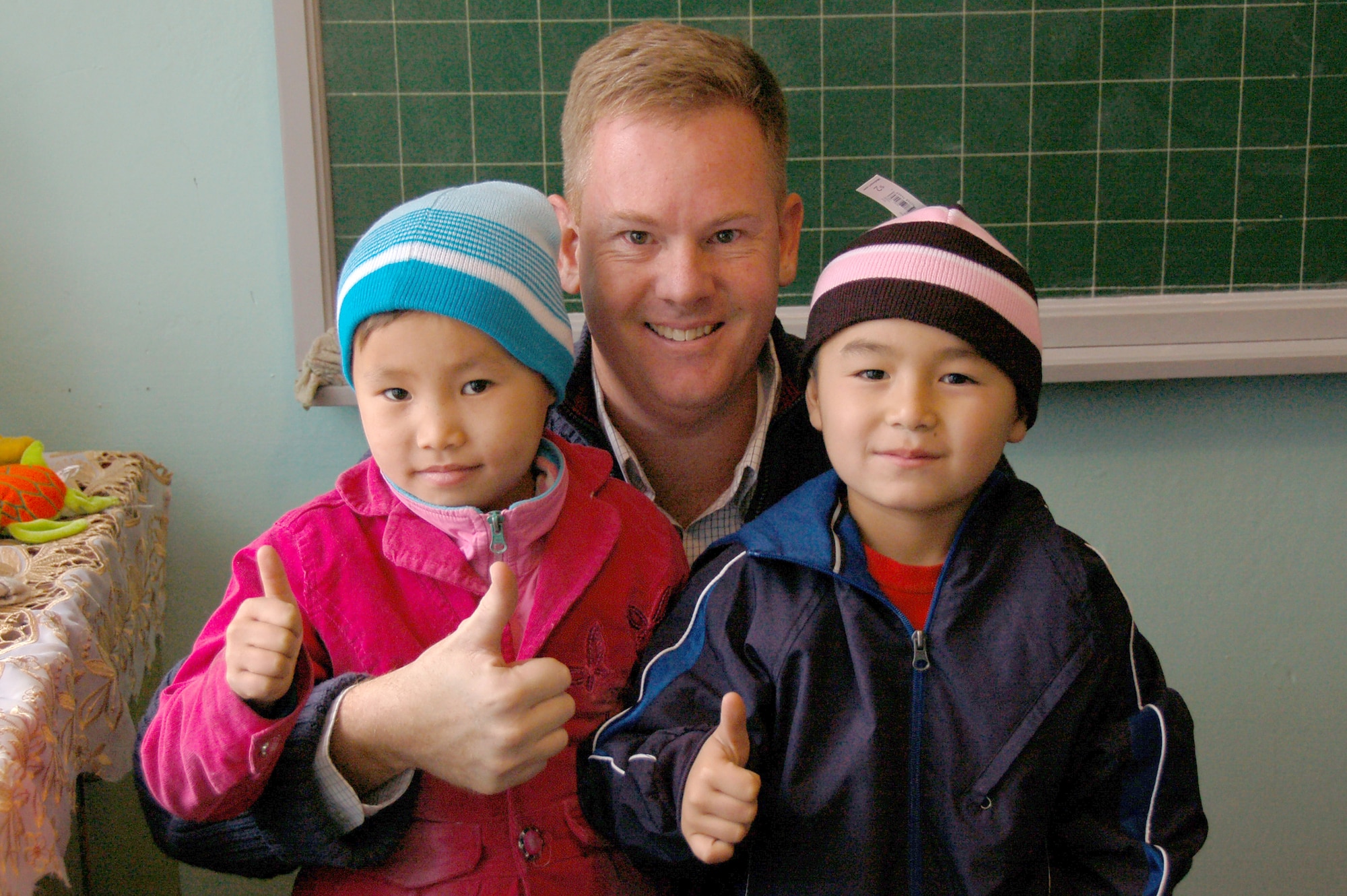 NIZHANCHUISK VILLAGE, Kyrgyzstan -- Lt. Col. Lee Landis, 376th Air Expeditionary Wing chief of safety, gives a 'thumbs-up' along with Nizhanchuisk Orphanage students after clothing them with new hats and jackets donated by the Blinn College Dental Hygiene Program students and faculty from Texas. Colonel Landis has been active with the orphanage while stationed at the Transit Center at Manas and reached out to his aunt and students at Blinn College for help with donations. (U.S. Air Force photo/Staff Sgt. Olufemi Owolabi)