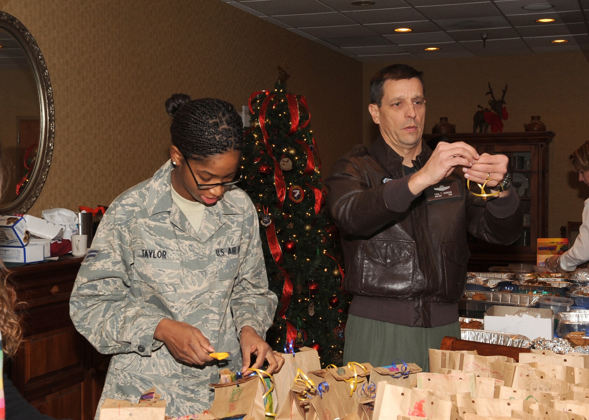 Brig. Gen. Paul Johnson, 355th Fighter Wing commander, assists Airman 1st Class Katrina Taylor, 355th Communications Squadron, and all the other volunteers, with tying and curling ribbon here Dec. 9. During the annual Davis-Monthan Cookie Crunch cookie drive, members of the D-M community volunteered their time to wrap and pack holiday cookies for Airmen living in the dormitories. Cookie donations were made from all over the base as well as from members of the Tucson community. (U.S. Air Force photo/Airman Jerilyn Quintanilla)
