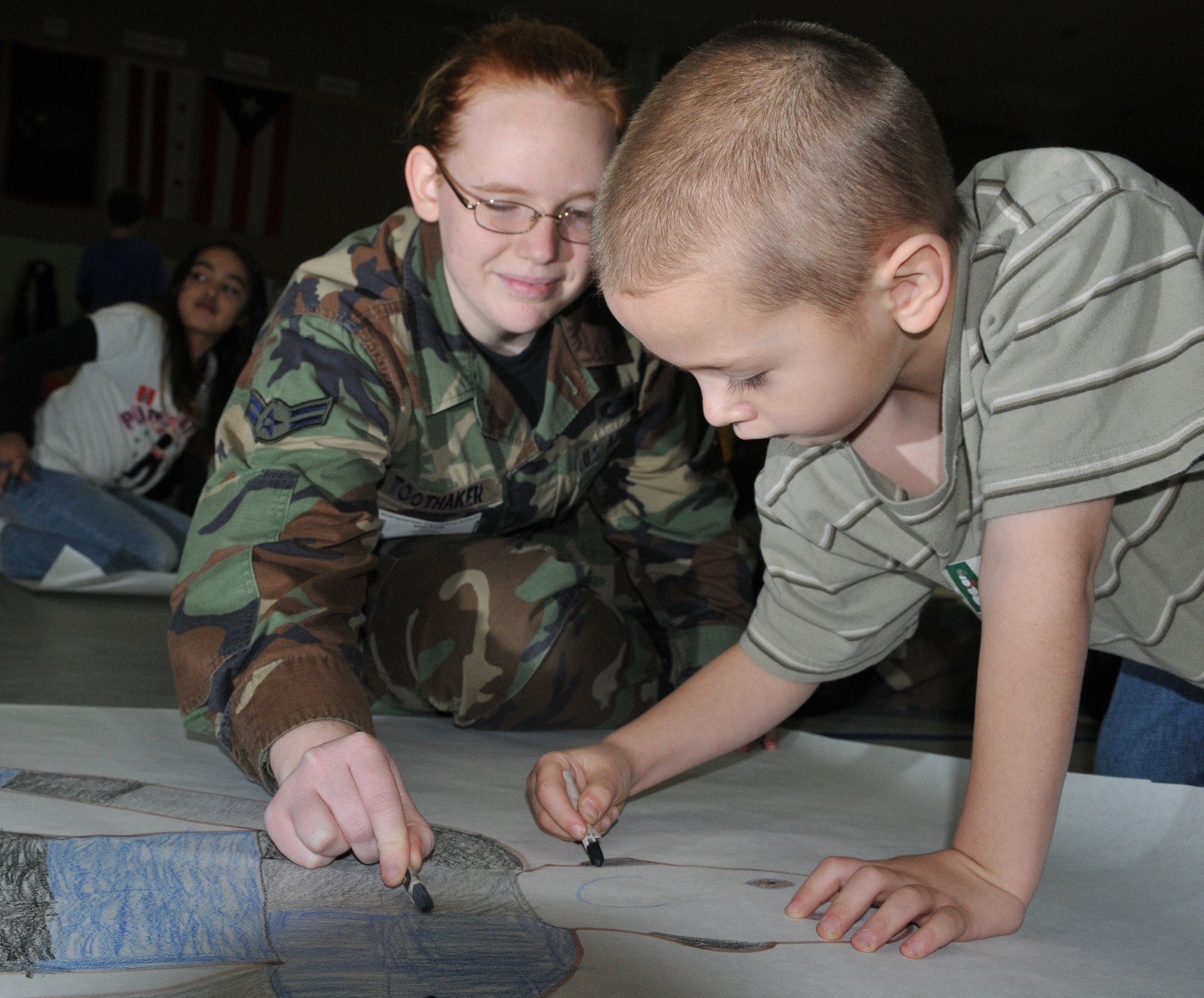 SPANGDAHLEM AIR BASE, Germany -- Airman 1st Class Tonya Toothaker, 606th Air Control Squadron, helps 7-year-old Zachary Collins make a life-size poster of himself Dec. 9 during the "Hugs for the Holidays" event in the Spangdahlem Elementary School gym to send to his father, Staff Sgt. George Collins, 52nd Aircraft Maintenance Squadron, who is currently deployed. The "Hugs for the Holidays" program is for students at SES to send replicas of themselves to family members who are deployed or TDY during the holidays. (U.S. Air Force photo/Airman 1st Class Nick Wilson)