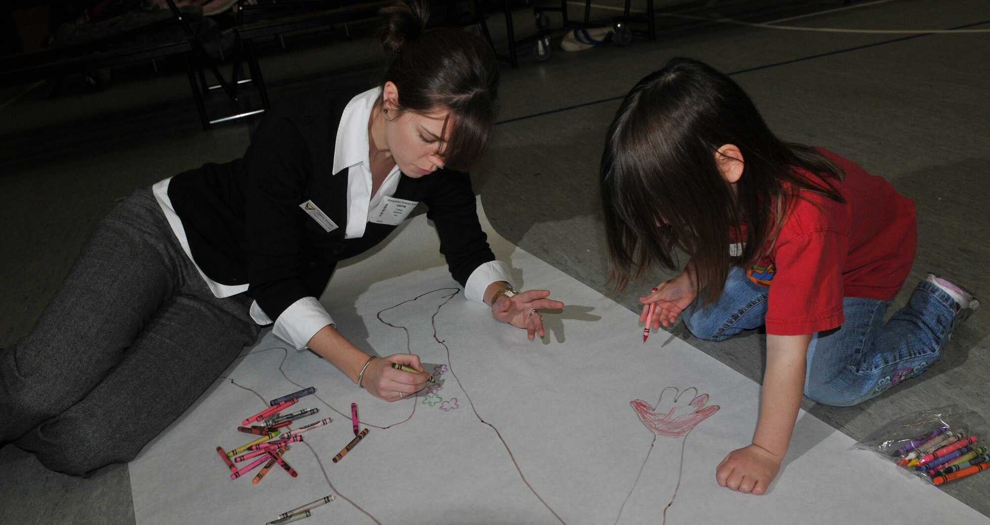 SPANGDAHLEM AIR BASE, Germany -- Lindsay Simmons, 52nd Force Support Squadron, helps 5-year-old Katarina Witham make a life-size poster of herself Dec. 9 during the "Hugs for the Holidays" event in the Spangdahlem Elementary School gym to send to her mother, Tech. Sgt Katarina Withum, 52nd Operation Support Squadron, who is currently deployed. The "Hugs for the Holidays" program is for students at SES to send replicas of themselves to family members who are deployed or TDY during the holidays. (U.S. Air Force photo/Airman 1st Class Nick Wilson)