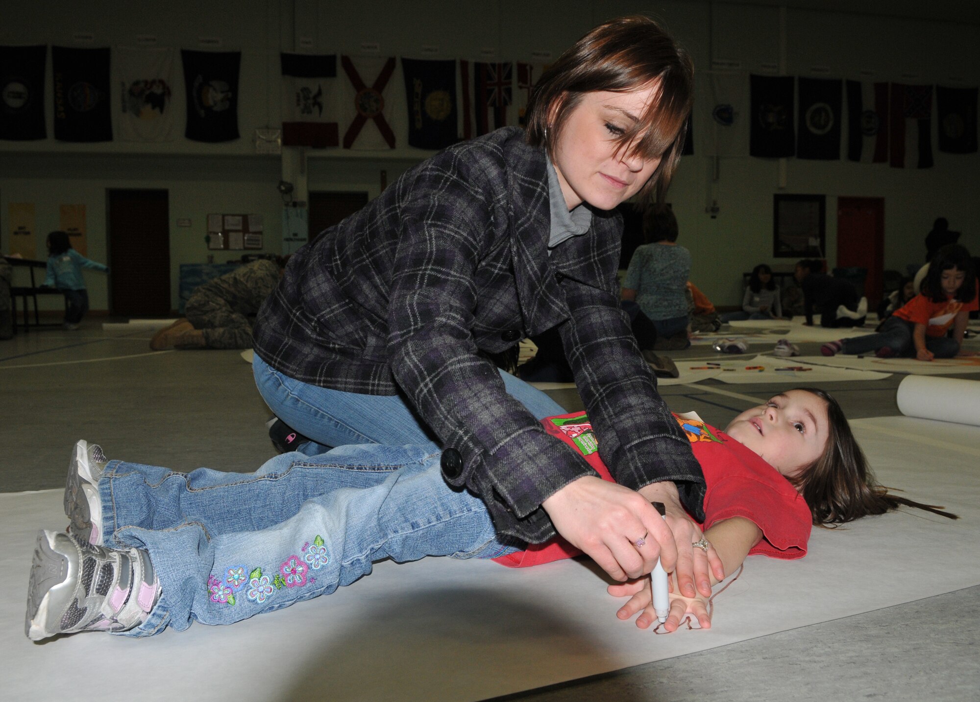 SPANGDAHLEM AIR BASE, Germany --Mindy Lundrum, a Saber volunteer, helps 5-year-old Katarina Witham make a life-size poster of herself Dec. 9 during the "Hugs for the Holidays" event in the Spangdahlem Elementary School gym to send to her mother, Tech. Sgt. Katarina Withum, 52nd Operation Support Squadron, who is currently deployed. The "Hugs for the Holidays" program is for students at SES to send replicas of themselves to family members who are deployed or TDY during the holidays. (U.S. Air Force photo/Airman 1st Class Nick Wilson)