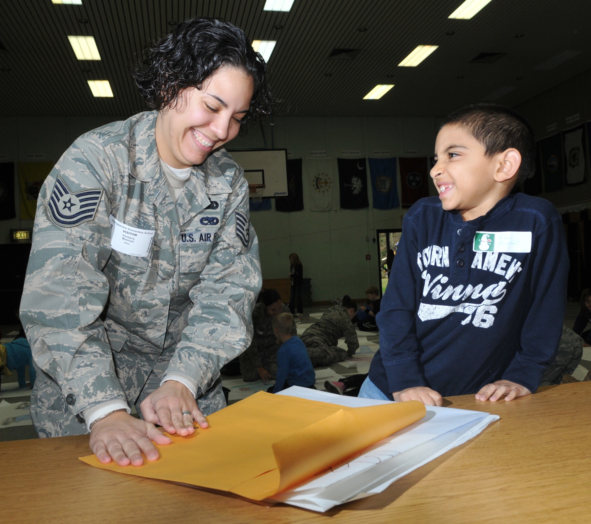 SPANGDAHLEM AIR BASE, Germany -- Tech. Sgt. Kimberly Marshall, 52nd Munitions Maintenance Group, helps her 8-year-old son, Ajani, package a life-size poster of himself during the "Hugs for the Holidays" event in the Spangdahlem Elementary School gym Dec. 9. Ajani plans to send the poster to his father, Tech. Sgt. Scott Marshall, 52nd Equipment Maintenance Squadron, currently at the Kisling NCO Academy in Kapaun Air Station, Germany. The "Hugs for the Holidays" program is for students at SES to send replicas of themselves to family members who are deployed or TDY during the holidays. (U.S. Air Force photo/Airman 1st Class Nick Wilson)