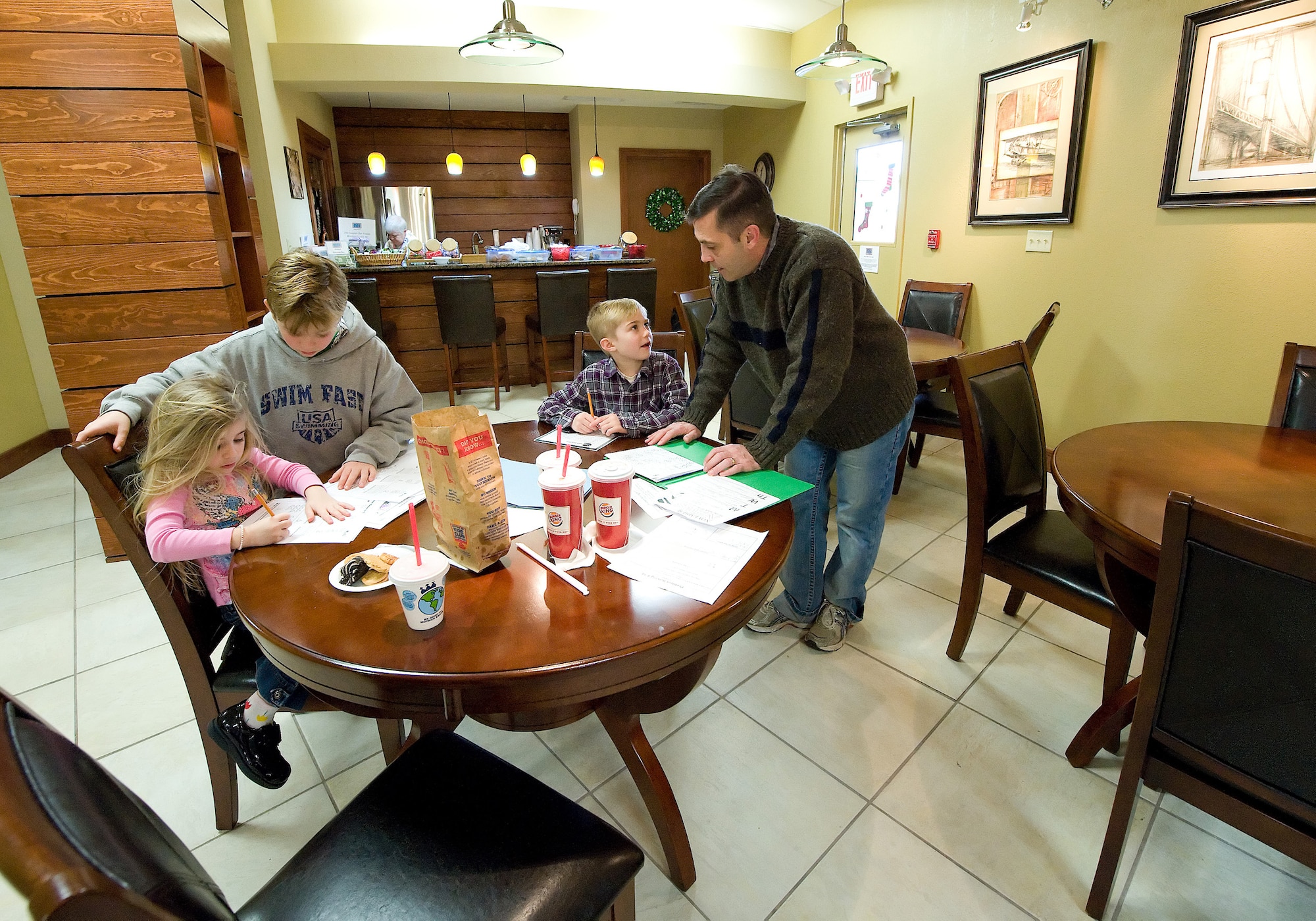 Army Col. Lars Braun helps his kids, (left to right) Ainsley, 5; Hunter, 9; and Joshua, 7, with their homework while waiting for a space available flight at the USO Lounge in the Dover Air Force Base Passenger Terminal. The lounge is open to all Department of Defense ID holders.  (U.S. Air Force photo/Jason Minto)