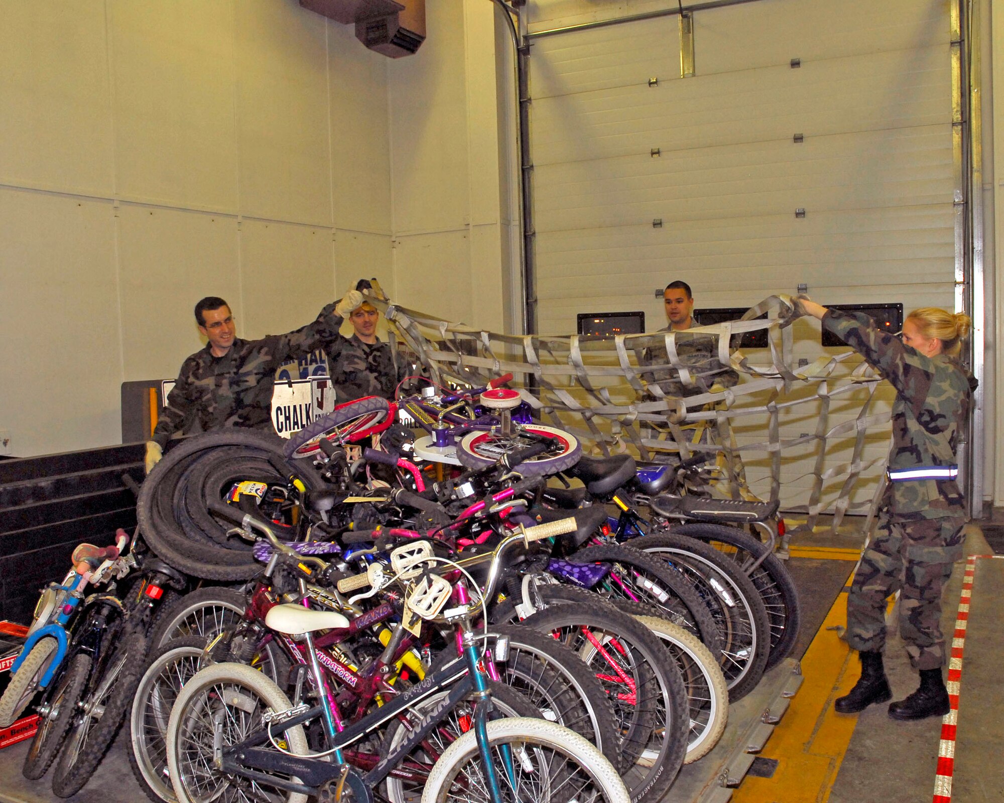 (Left to right) Alaska Air Guardsmen Staff Sgt. Woody Miller, Senior Airman John Darnall, Senior Airman Ryan Pierce and Tech. Sgt. Summer Rehak from the 176th Logistics Readiness Squadron pulls a top net over a pallet of refurbished bicycles on December 6, 2009. The bikes will be airlifted to Afghanistan to be given to disadvantaged children. (Alaska Air National Guard photo/Tech. Sgt. Shannon Oleson)