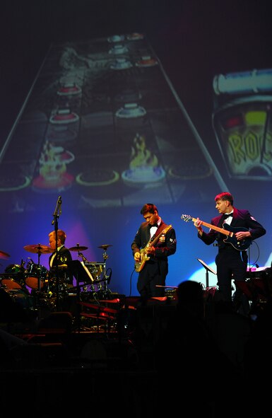 OFFUTT AIR FORCE BASE, Neb.- Staff Sgt. Timothy Rogers (right) and Senior Airman Daniel Santos (left), thrash out the "We Three Kings" song on their electric guitars while keeping sync with the Guitar Hero playing behind them during the Heartland of America Band's Holiday concert at the Holland Performing Arts Center in Omaha, Neb., Dec. 10. U.S. Air Force Photo by Josh Plueger