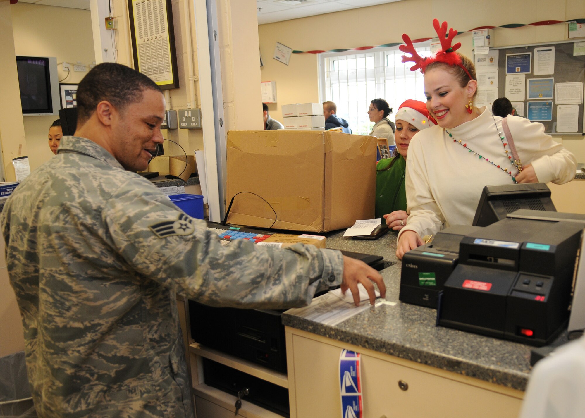 RAF MILDENHALL, England – Senior Airman Denny Williams, 100th Communication Squadron postal clerk, assists Marissa Nunnes and Alex House with an outgoing package at the RAF Mildenhall Post Office Dec. 15. The post office will be providing extended hours during the holiday season. Outgoing mail will be open from 8:30 a.m. to 5 p.m. Monday through Friday and 9 a.m. to 1 p.m. Saturday. The pick-up window hours are 8 a.m. to 6 p.m Monday through Friday and 9 a.m to 1 p.m. Saturday. The post office will resume normal business hours Dec. 28. (U.S. Air Force photo/ Staff Sgt. Jerry Fleshman)