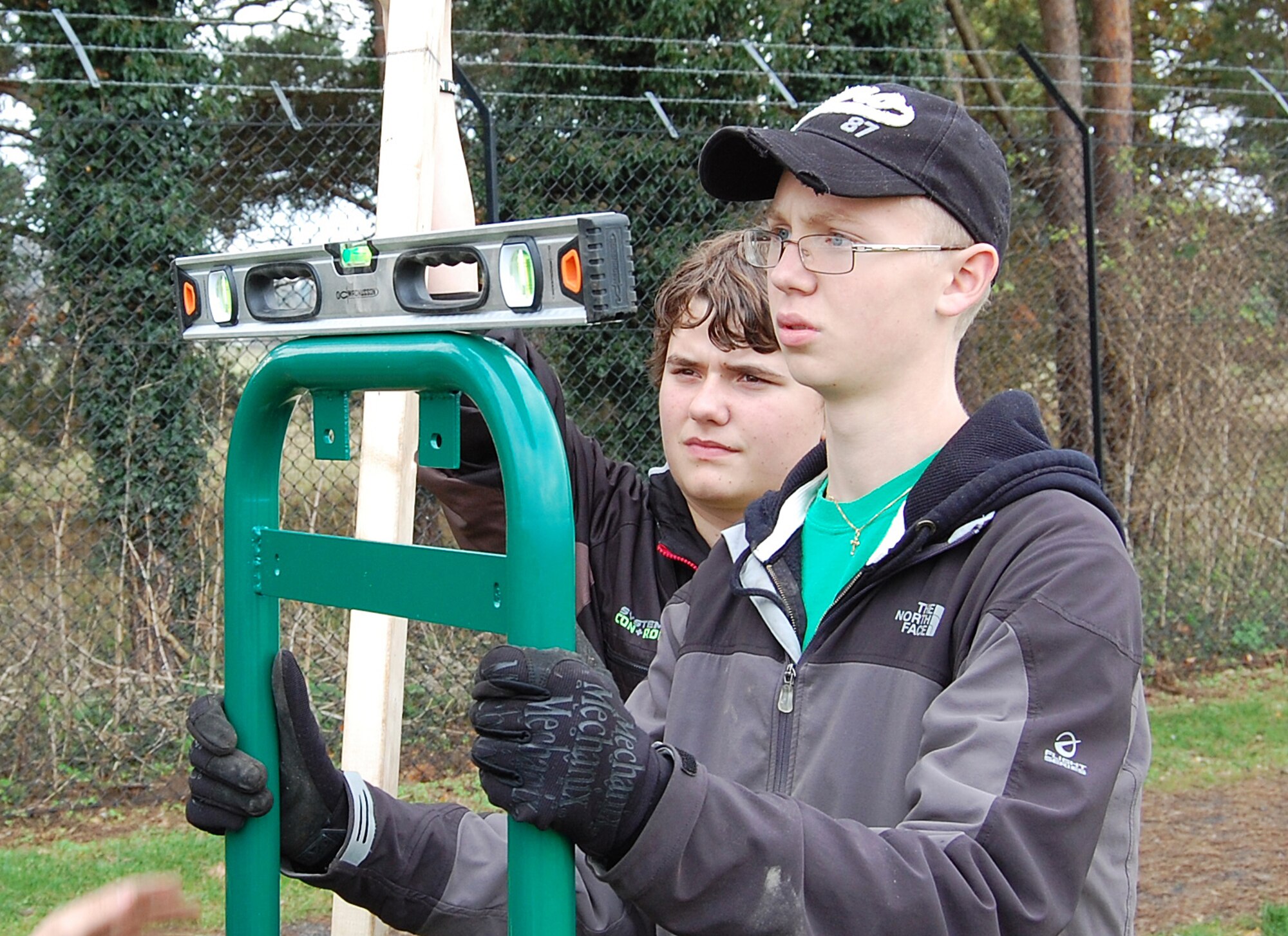 Joshua Kent (right) and Hayden Howard, eye a leveler to ensure the poles of one of the 15 new fitness stations along the RAF Lakenheath running trail are correctly fitted.  Joshua Kent, a boy scout with Troop 219 here, initiated this project to earn his Eagle Scout badge. (Photo by Tim Barlow) 