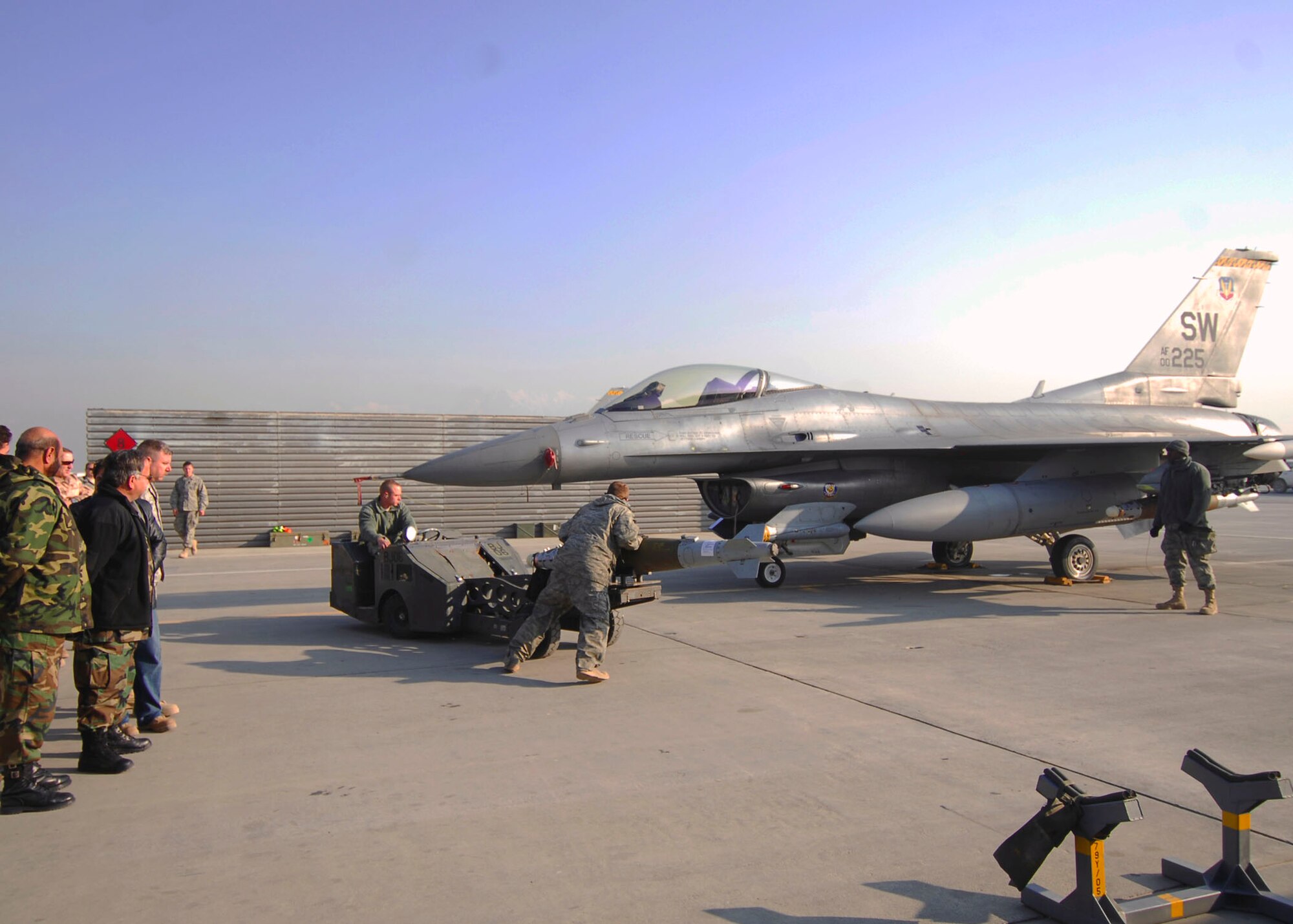 Staff Sgt. Sam Arpy, Weapons Load Crew leader and Des Moines, Iowa native, drives a “Bomb-lift Truck” while Airman 1st Class John Ackerman, a Ft. Worth, Texas assists him to the “Bomb Rack” of an F-16 Fighting Falcon, Dec. 19, 2009.  Airman 1st Class Carl Jones, a Ft. Worth, Texas native (far right) spots Sergeant Arpy.  All Airmen are deployed from Shaw Air Force Base, S.C. and were demonstrating proper loading procedures for Afghan National Army Air Corps Brig. Gen. Abdul Wahab Wardak and other officials, Dec. 19, 2009.  (U.S. Air Force photo/Capt. David Faggard)