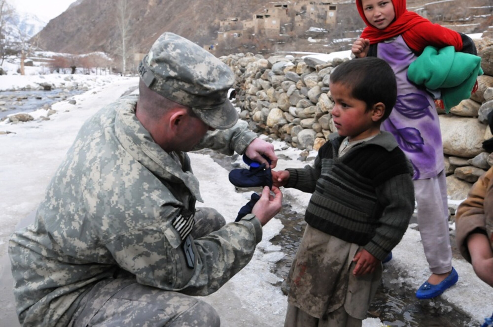 PANJSHIR PROVINCE, Afghanistan – Panjshir Provincial Reconstruction Team’s executive officer, Army Maj. Ian Murray, helps a young resident of Panjshir province’s Dara district into a new pair of mittens during a recent material assistance drop to the area in Afghanistan, Dec. 14. The PRT delivered coats, hats, gloves, school supplies and food to the district area after they helped assist in the recovery of a disabled truck owned by the PRT. (Air Force photo/Capt. John T. Stamm)