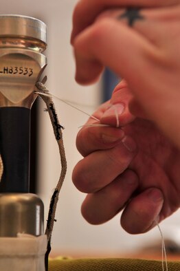 An Airman from the 4th Operations Support Squadron life support flight tacks back-up firing lanyards to a mortar on a parachute container at Seymour Johnson Air Force Base, N.C., Dec. 15, 2009. The parachute is equipped with a cord on the bottom of the canopy that allows the canopy to open slower to prevent injury of aircrew members. (U.S. Air Force photo/Airman 1st Class Rae Perry)