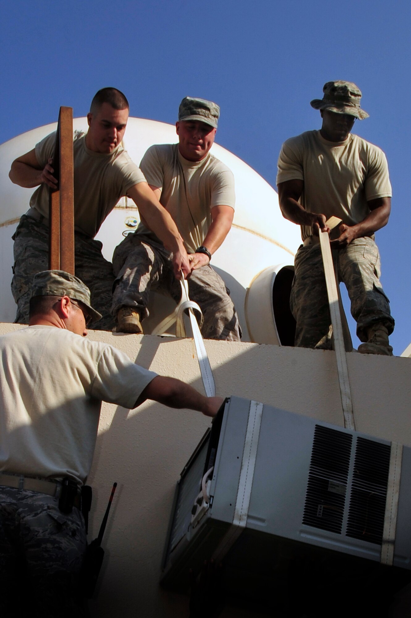 SOUTHWEST ASIA – Members of the 380th Expeditionary Civil Engineer Squadron heating ventilation and air conditioning hoist a replacement air conditioner unit up to the roof Dec. 17, 2009. The air conditioner was wall-mounted by the HVAC Airmen and is used to cool communications equipment. (U.S. Air Force photo/Tech. Sgt. Charles Larkin Sr)