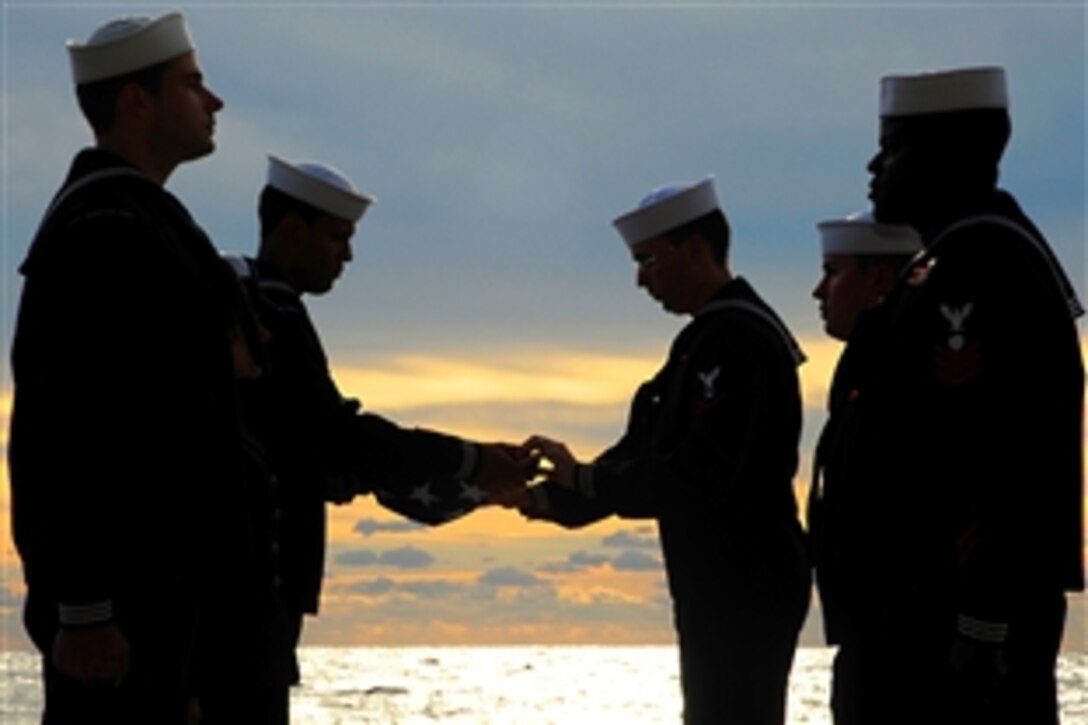 U.S. Navy Seaman Josue Fernandez-Lopez,left, and Petty Officer 2nd Class Theo Beasley fold the American flag while pall bearers stand at attention during a burial at sea ceremony aboard the USS Gunston Hall in the Atlantic Ocean, Dec. 12, 2009. 
