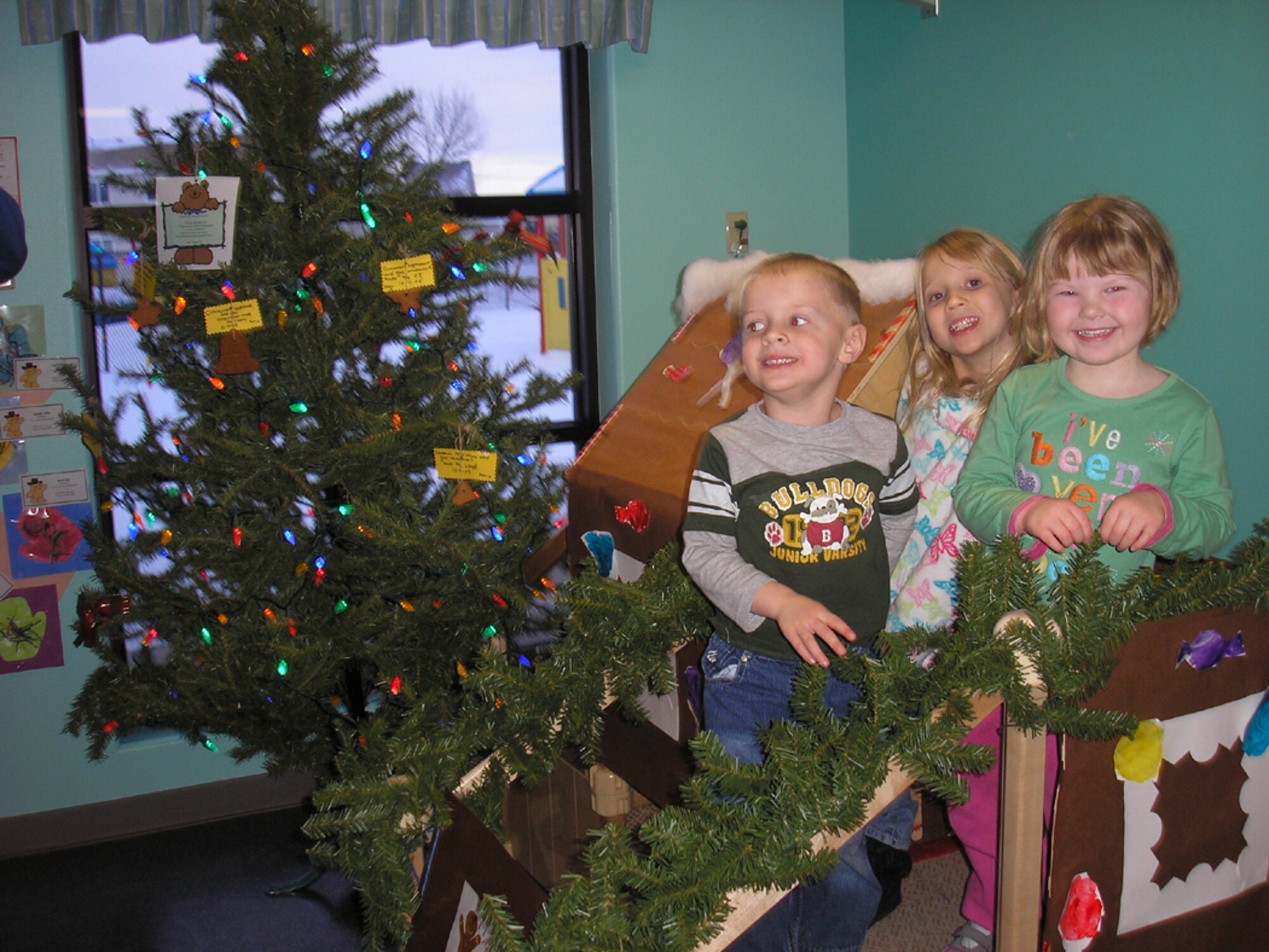 Pre-schoolers Jordan Willets, Chloe Piatt and Felicity Sakura are all smiles at the Christmas tea party at the Child Development Center Dec. 11. The children in the 14 classrooms at the center made the decorations that adorned the tree and walls. (Courtesy photo)