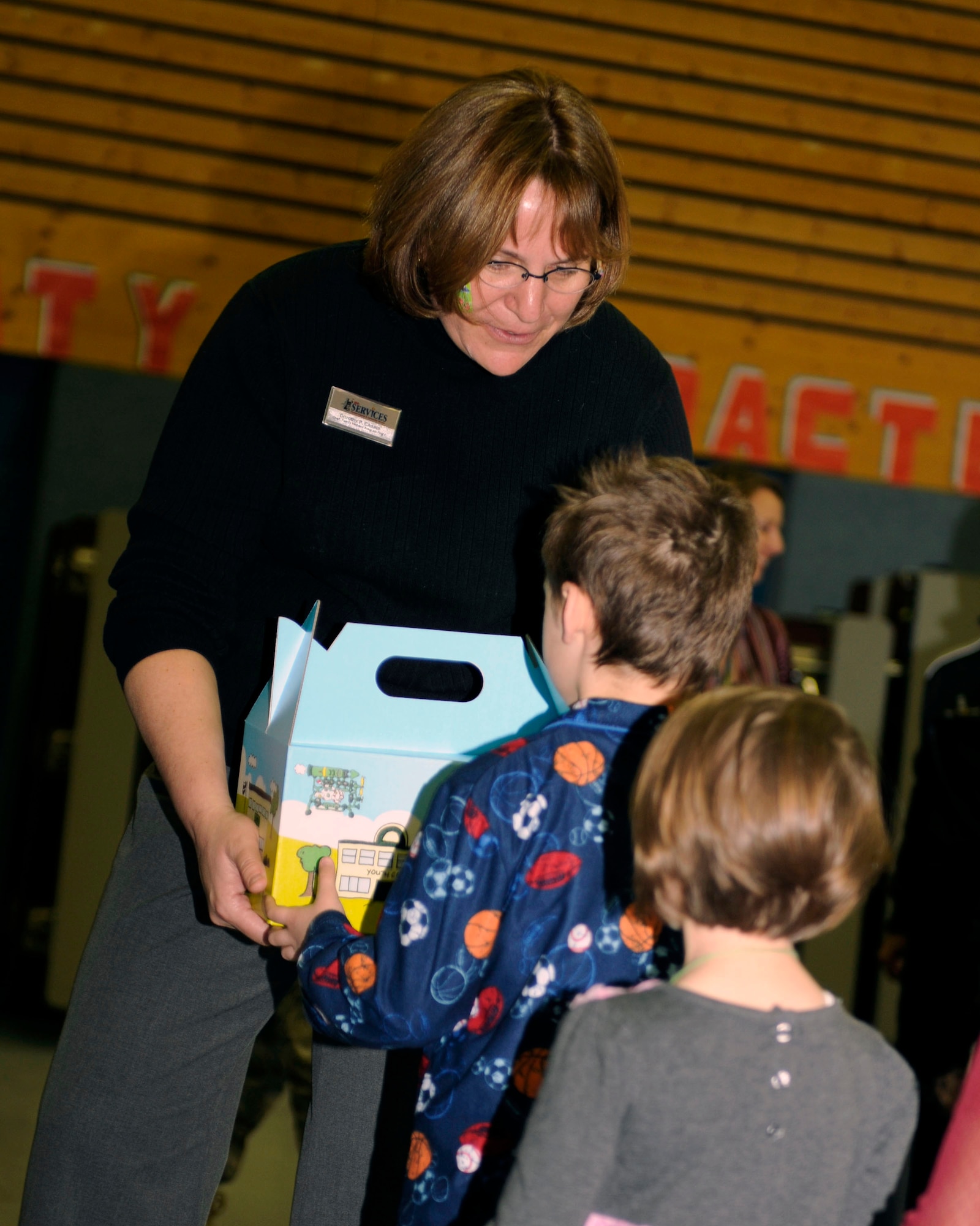 Dorothy Choate, 86th Services Squadron, family member program flight chief, hands out Cuzzie Cares Deployment Kits at Ramstein Elementary School, Ramstein Air Base, Germany, Dec. 17, 2009. Cuzzie, designed by Mr. Trevor Romain, is an inventive bear that creates flying machines with the help of his ground crew and is the centerpiece of a new kit designed to comfort school-age children during deployments. (U.S. Air Force photo by Airman 1st Class Brea Miller)