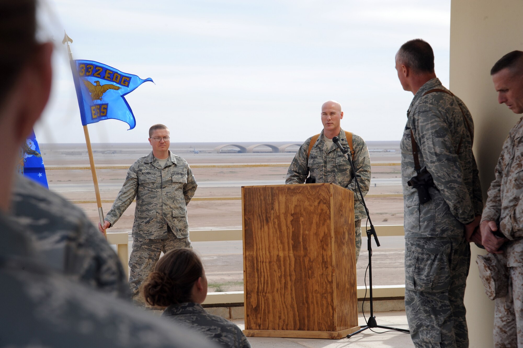 AL ASAD AIR BASE, Iraq -- Air Force Master Sgt. Christopher Alden (left) stands by with the unit guidon as the new commander of the 532nd Expeditionary Operations Support Squadron, Lt. Col. Barry Dickey (center), speaks about the future of Al Asad airfield during the assumption of command ceremony Dec. 15, 2009. The airfield was previously operated by the U.S. Marine Corps, but due to the drawdown, the Air Force has taken over these responsibilities. (U.S. Air Force photo/Master Sgt. Trish Bunting)