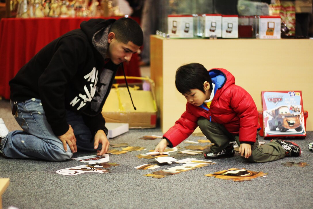 Sgt. Mark Prado assembles a puzzle with a Japanese boy during the Yahata Children’s Home visit here Dec. 19. Service members and families from Marine Wing Support Squadron 171 sponsored the children for a fun-filled day of Holiday gift giving and fellowship aboard the air station.