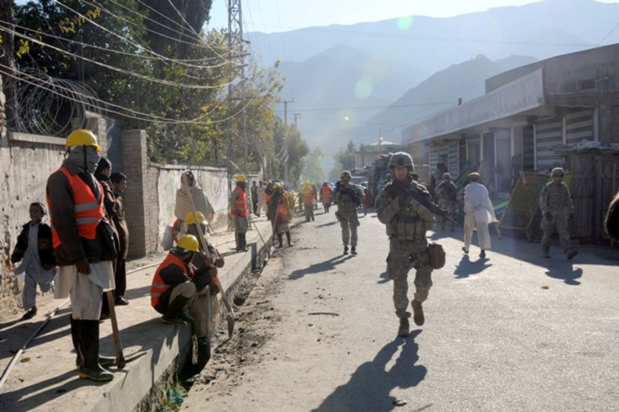 KUNAR PROVINCE, Afghanistan – Local workers cleaning the streets in downtown Asadabad watch a Provincial Reconstruction Team-Kunar patrol conduct a final quality assurance and quality check on a new 4-kilometer road through the provincial capital prior to a dedication ceremony, recently. The Provincial Reconstruction Team-Kunar engineers did the check to ensure the Kunar Construction Company did a good job building the road. The project took nearly one year and approximately $1 million to complete. The hope for the new road is it will continue to spur economic development and job growth in the city. More than 50 provincial leaders and tribal elders gathered at the ceremony site after the QA/QC check to do the ribbon cutting ceremony. (U.S. Air Force photo/Tech. Sgt. Brian Boisvert)