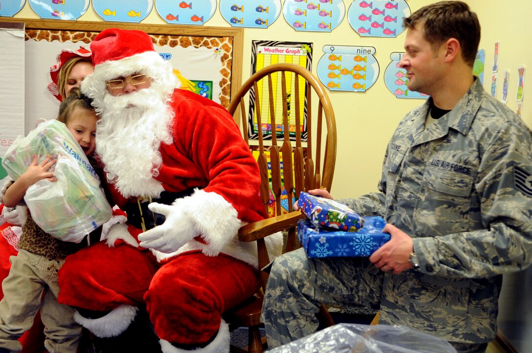 ELLSWORTH AIR FORCE BASE, S.D.-- Santa gets a hug from a child while Tech Sergeant Justin Cooke, 28th Operations Support Squadron helps distribute presents at the Youth and Family Services child care center in Rapid City, S.D., Dec. 17. YFS staff provided the names and ages of infants, toddlers and preschool-aged children in their program to 28th Operations Group members, who then purchased and wrapped gifts for every child. (US Air Force photo/Airman 1st Class Corey Hook)